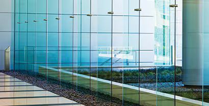 Modern glass office building facade with blue reflections and landscaped walkway