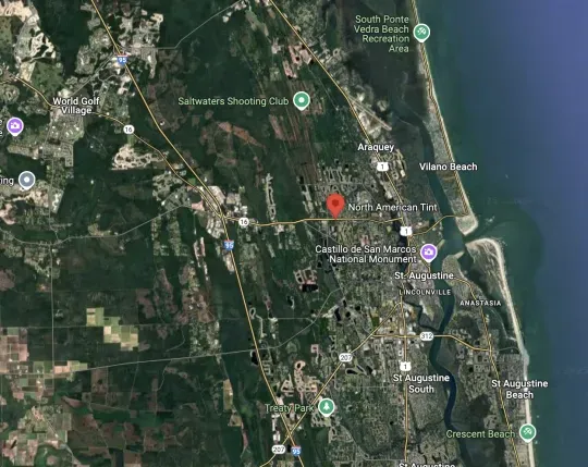 Satellite map of a coastal town with roads, buildings, and a red location pin near the shoreline