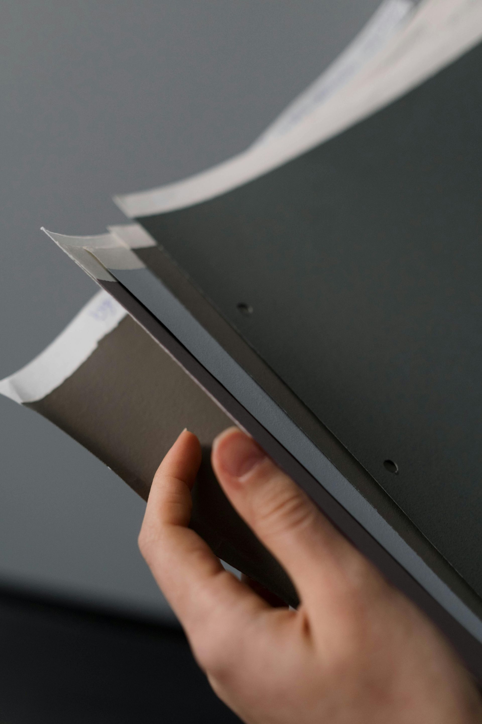 Hand holding a gray notebook or folder with white pages flipping open