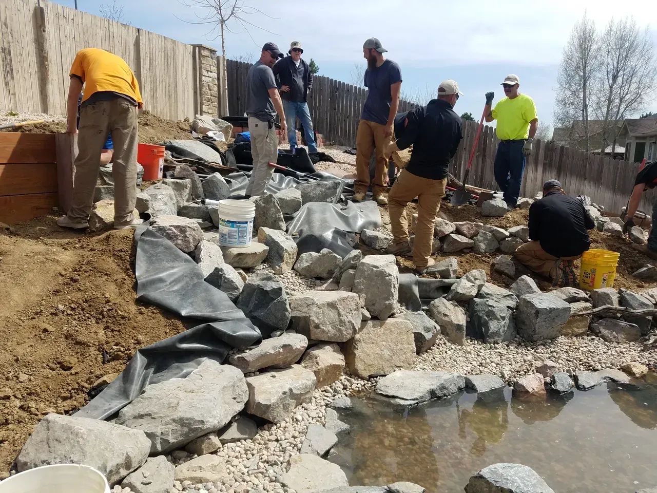 A group of men are working on a rocky area next to a pond.