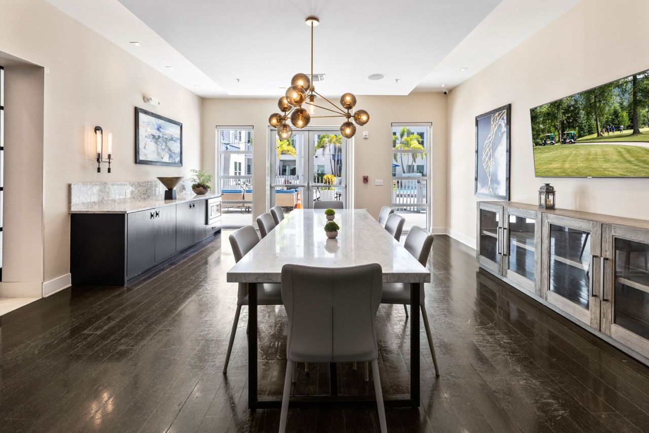 Bright community room with a long marble dining table, chairs, and built-in cabinets.
