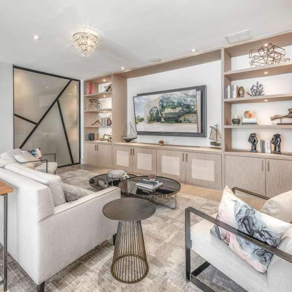 A modern living room with light wood shelving, a flat-screen TV, white sofas, and geometric accent glass panels.