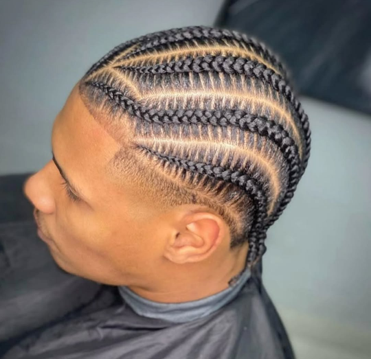 A man with braids in his hair is wearing a black cape.