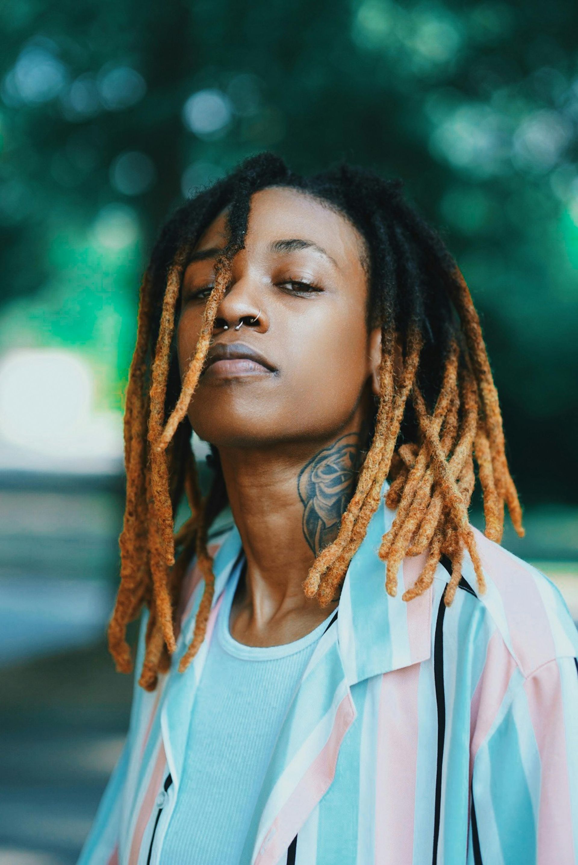 A woman with dreadlocks and a tattoo on her neck is wearing a striped shirt.