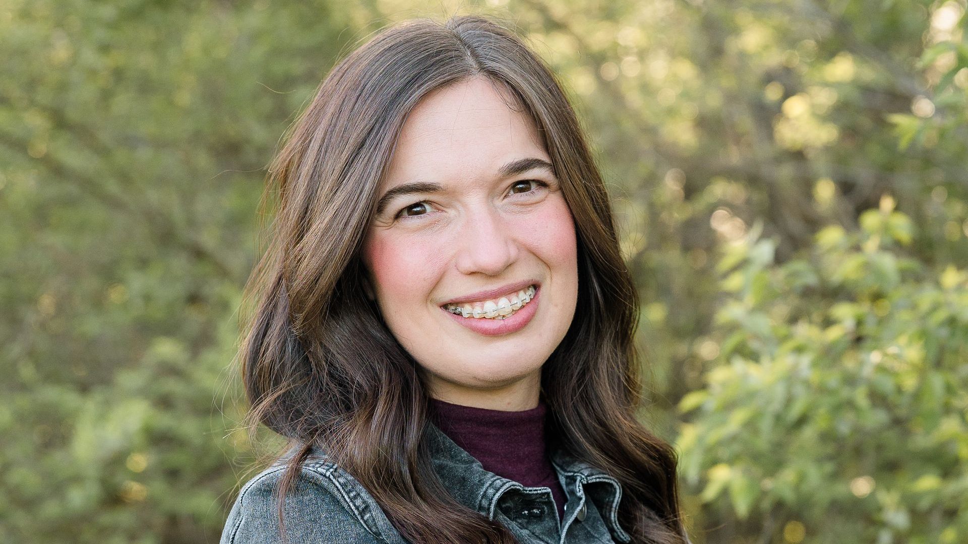 A woman is smiling for the camera while standing in front of a tree.
