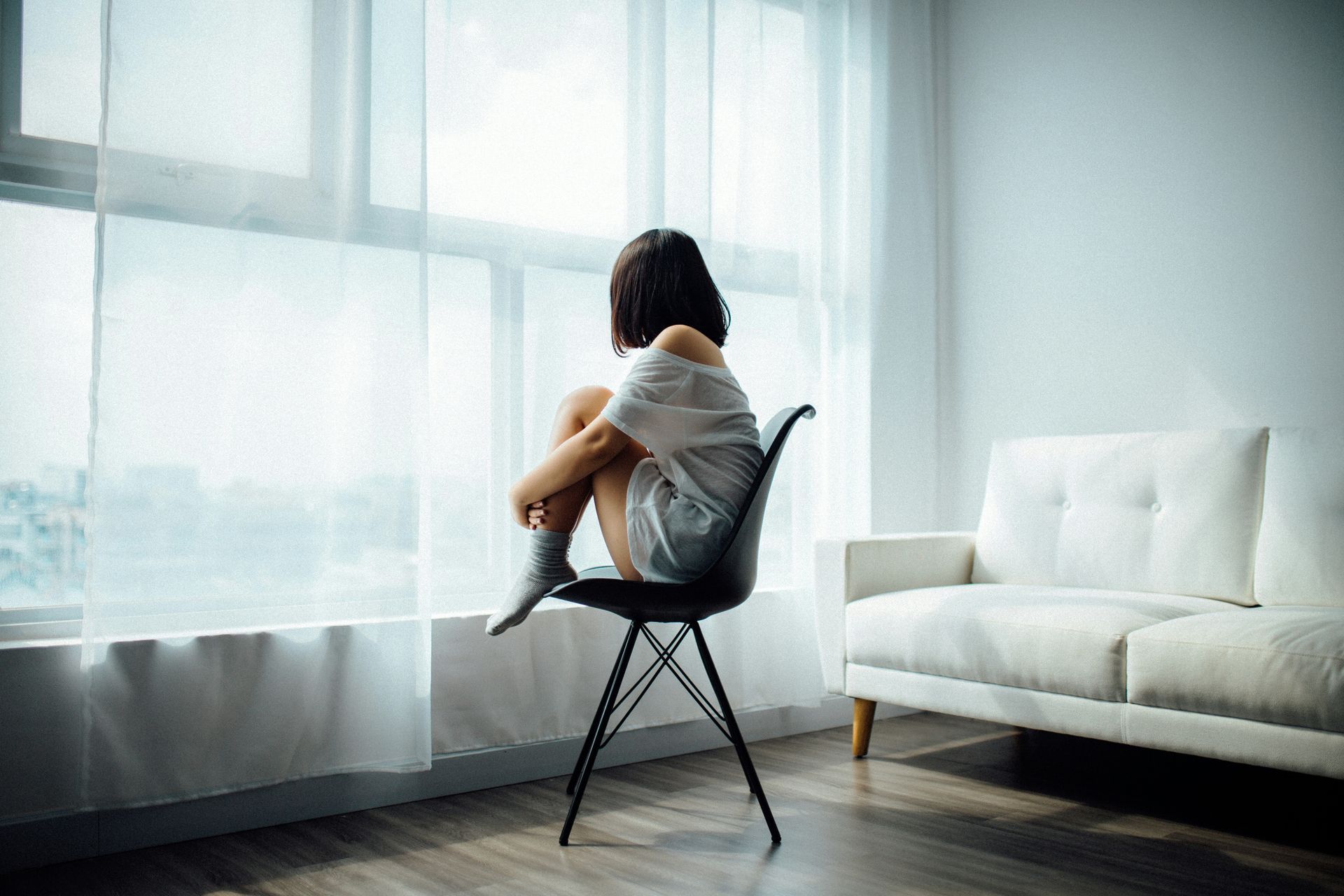 A woman is sitting in a chair looking out a window.