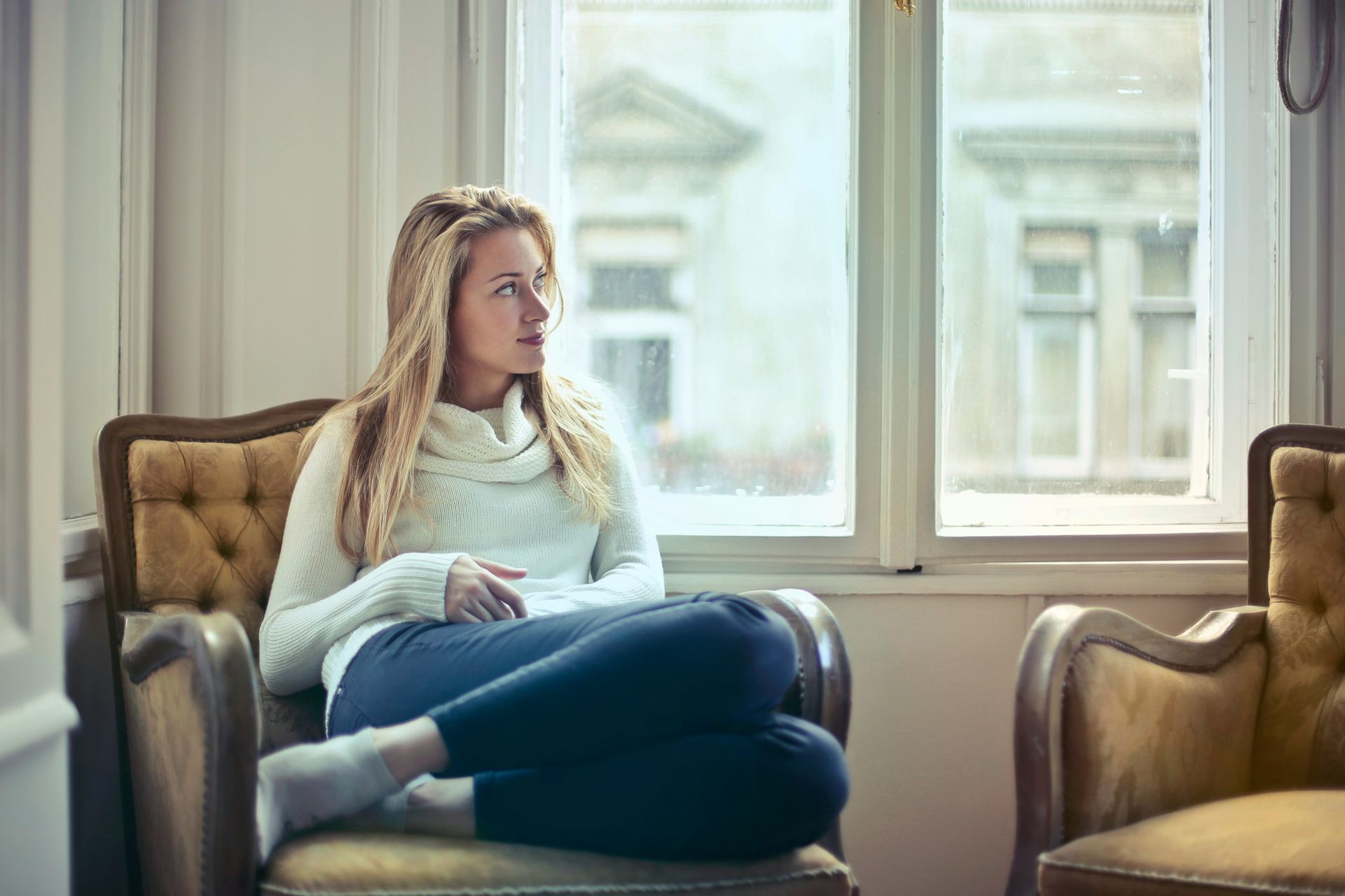 A woman is sitting in a chair in front of a window.