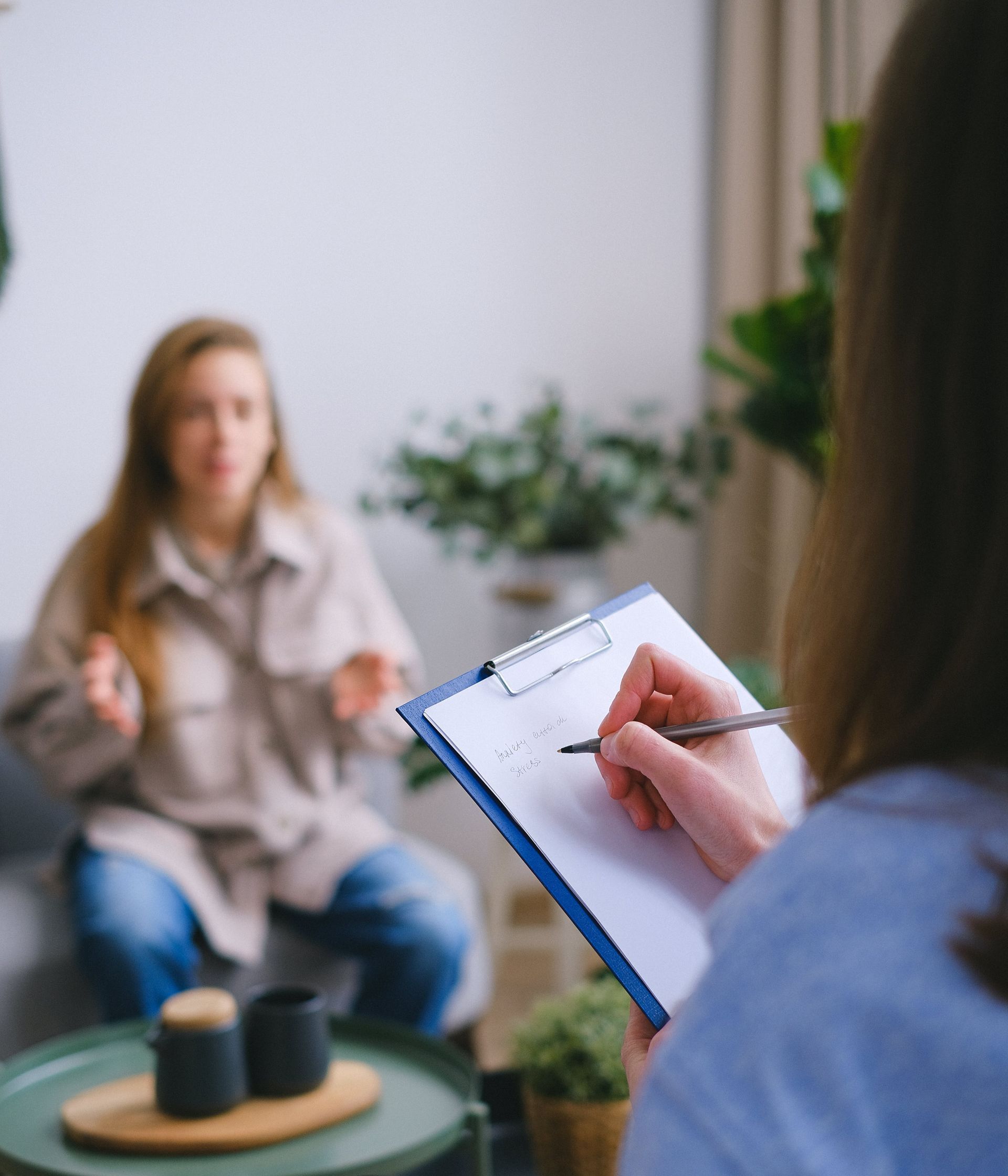 a woman is sitting on a couch talking while a therapist writes on a clipboard .