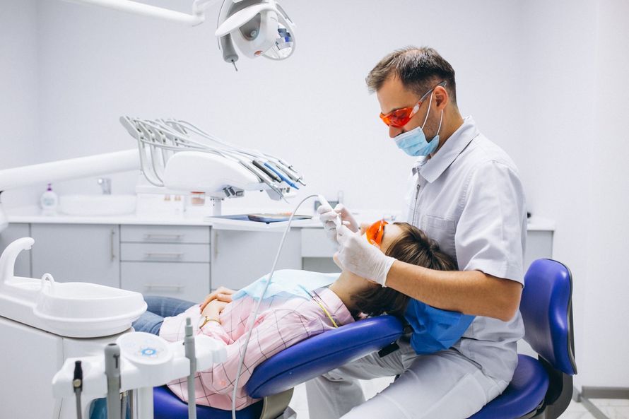 Dentista atendiendo a un paciente en un sillón. Ambos usan mascarillas y el paciente lleva gafas de seguridad.