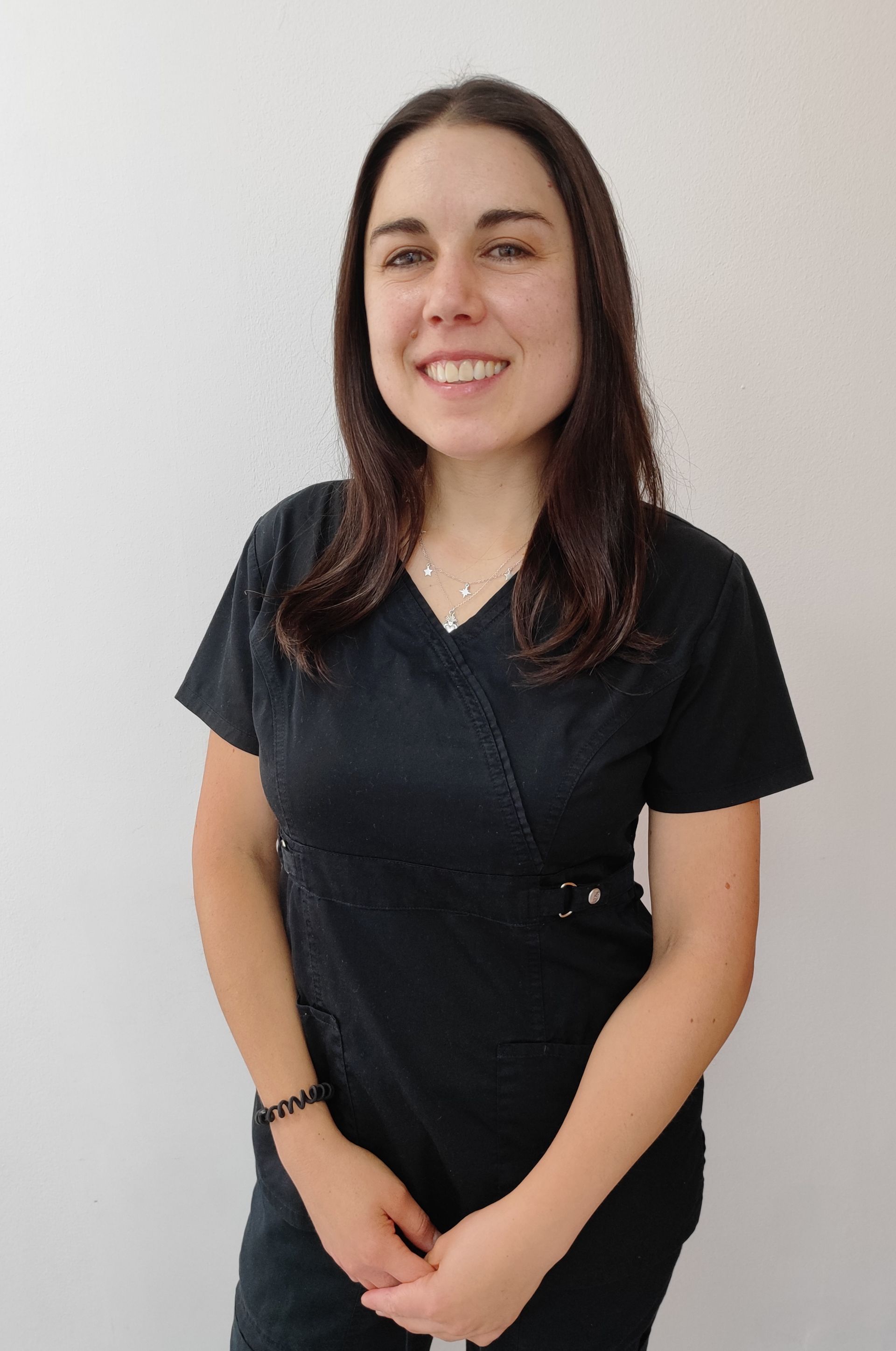 Una mujer vestida con un uniforme negro sonríe, parada frente a una pared blanca.