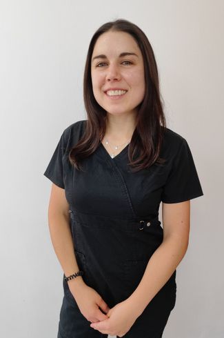 Una mujer vestida con un uniforme negro sonríe, parada frente a una pared blanca.