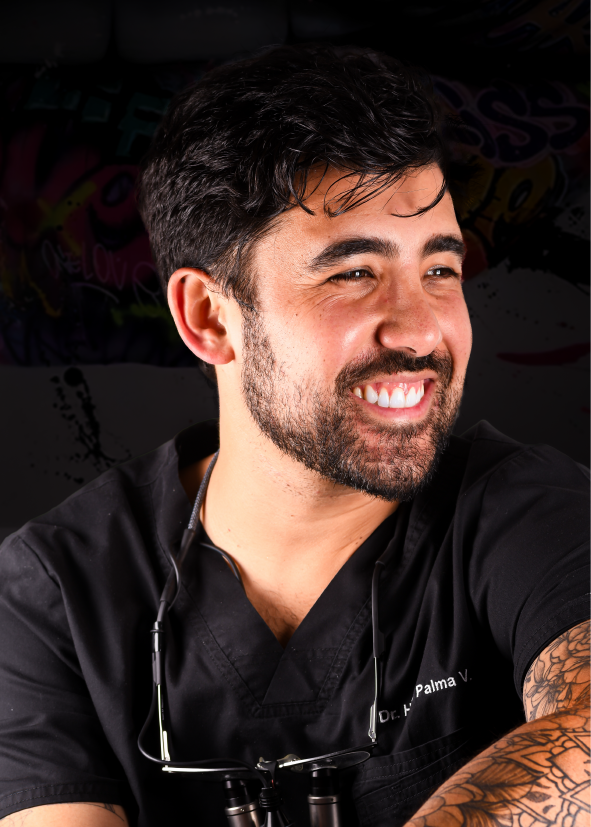 Hombre sonriente con uniforme médico negro y gafas al cuello, mirando fuera de cámara. Tatuaje visible en el brazo.