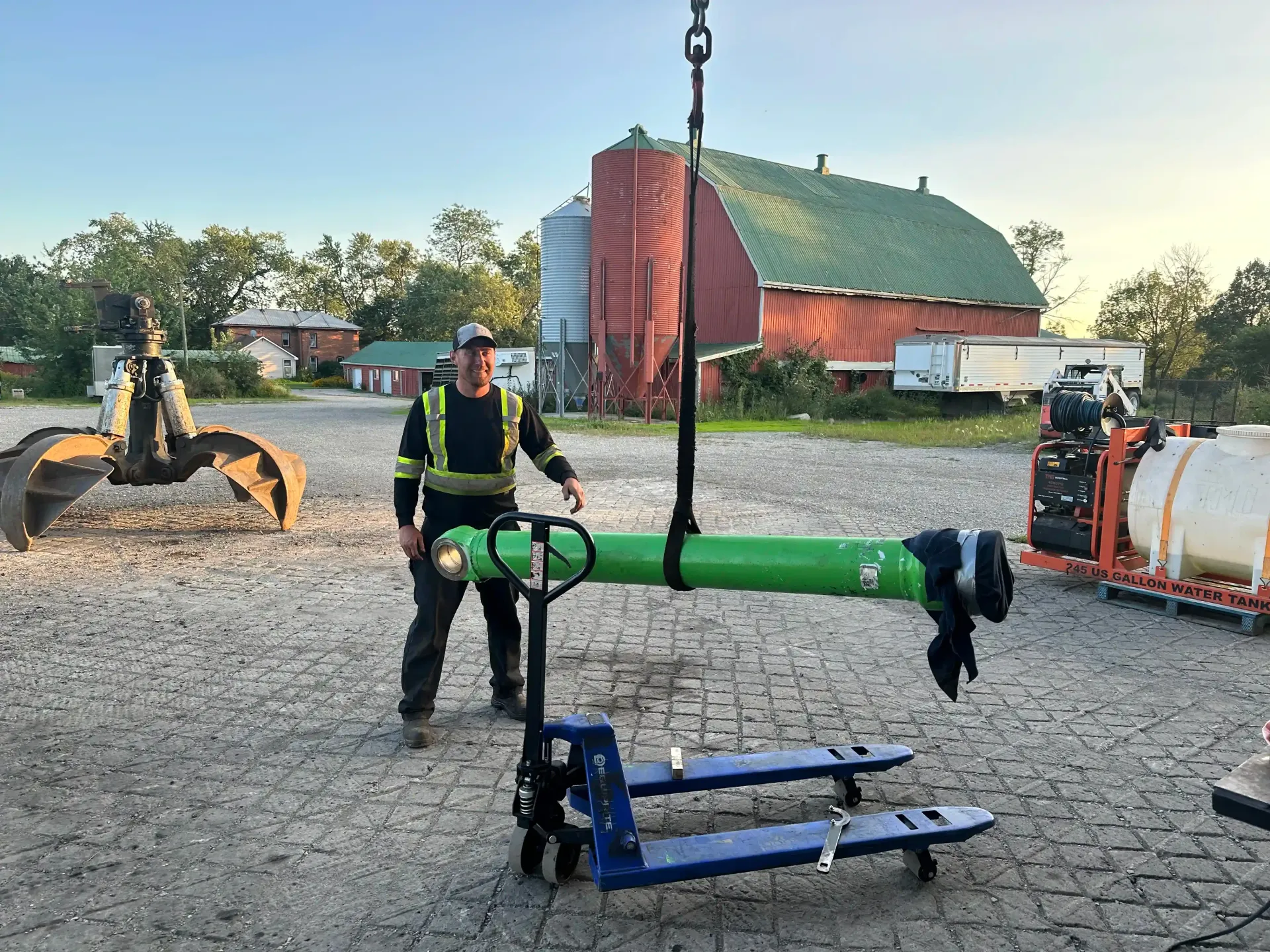 A man is standing next to a green pipe that is being lifted by a crane.