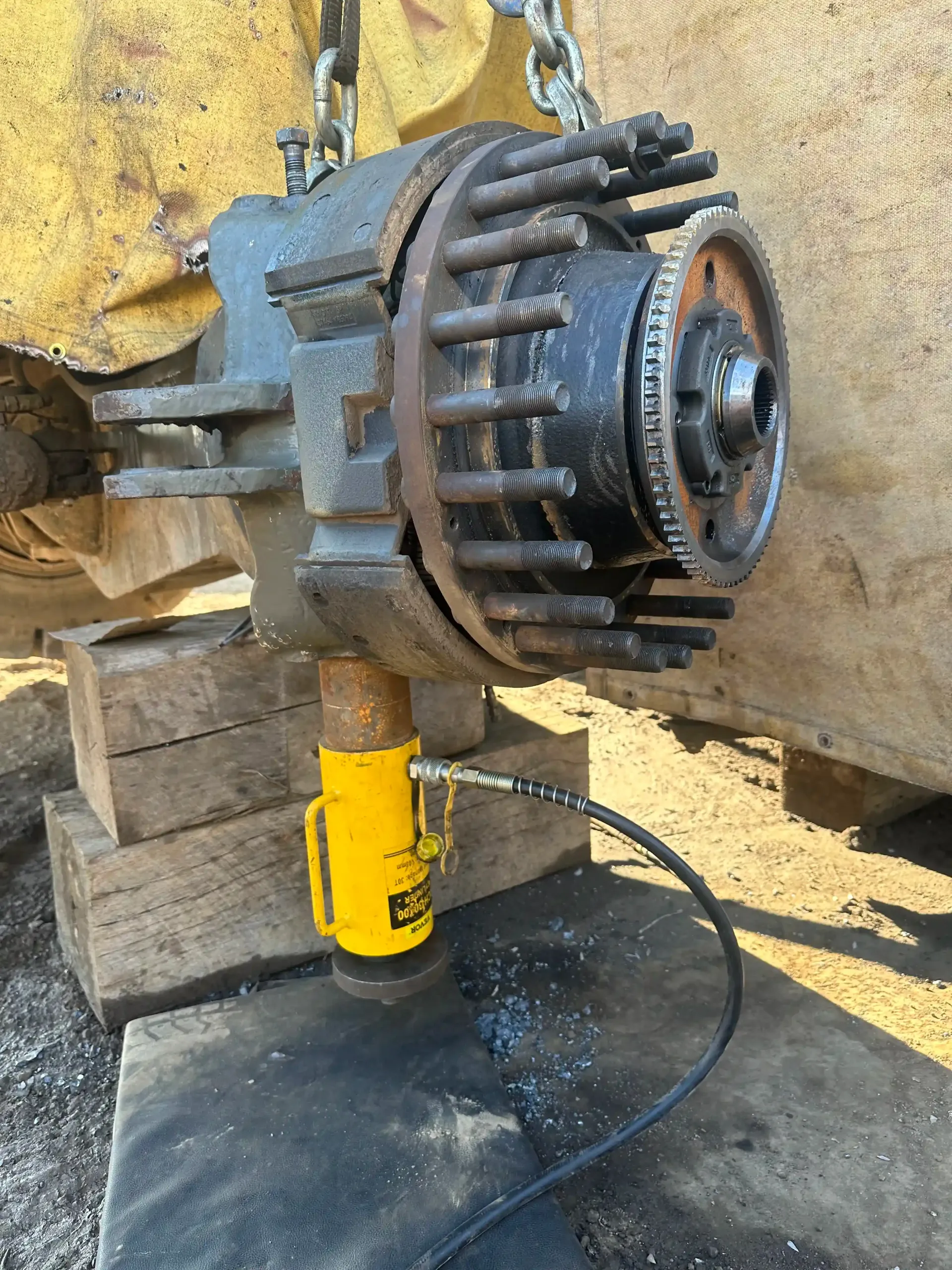 A large metal object is being lifted by a yellow hydraulic jack.