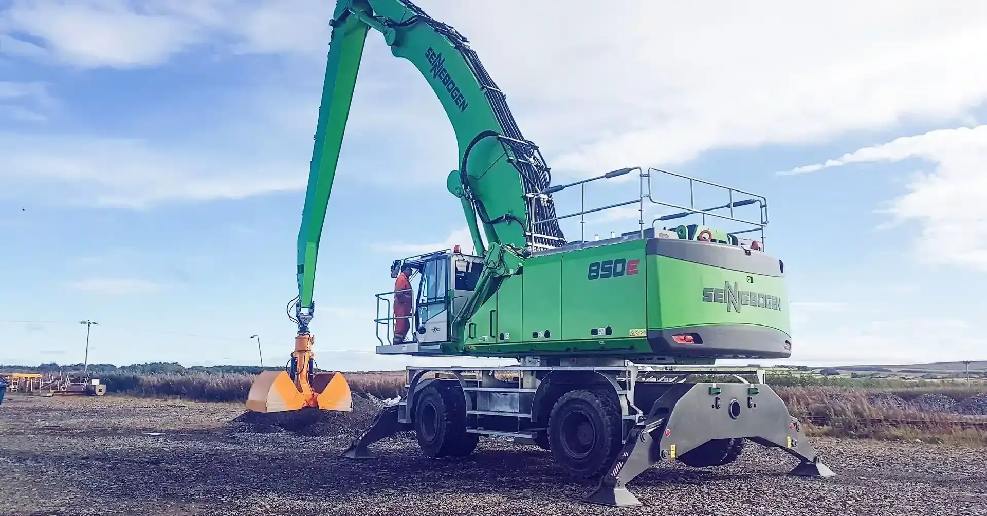 A large green excavator is sitting on top of a gravel field.