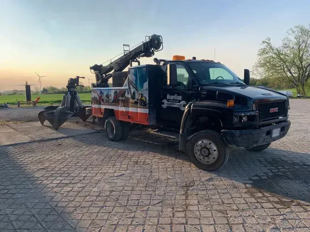 A tow truck with a crane attached to it is parked in a parking lot.