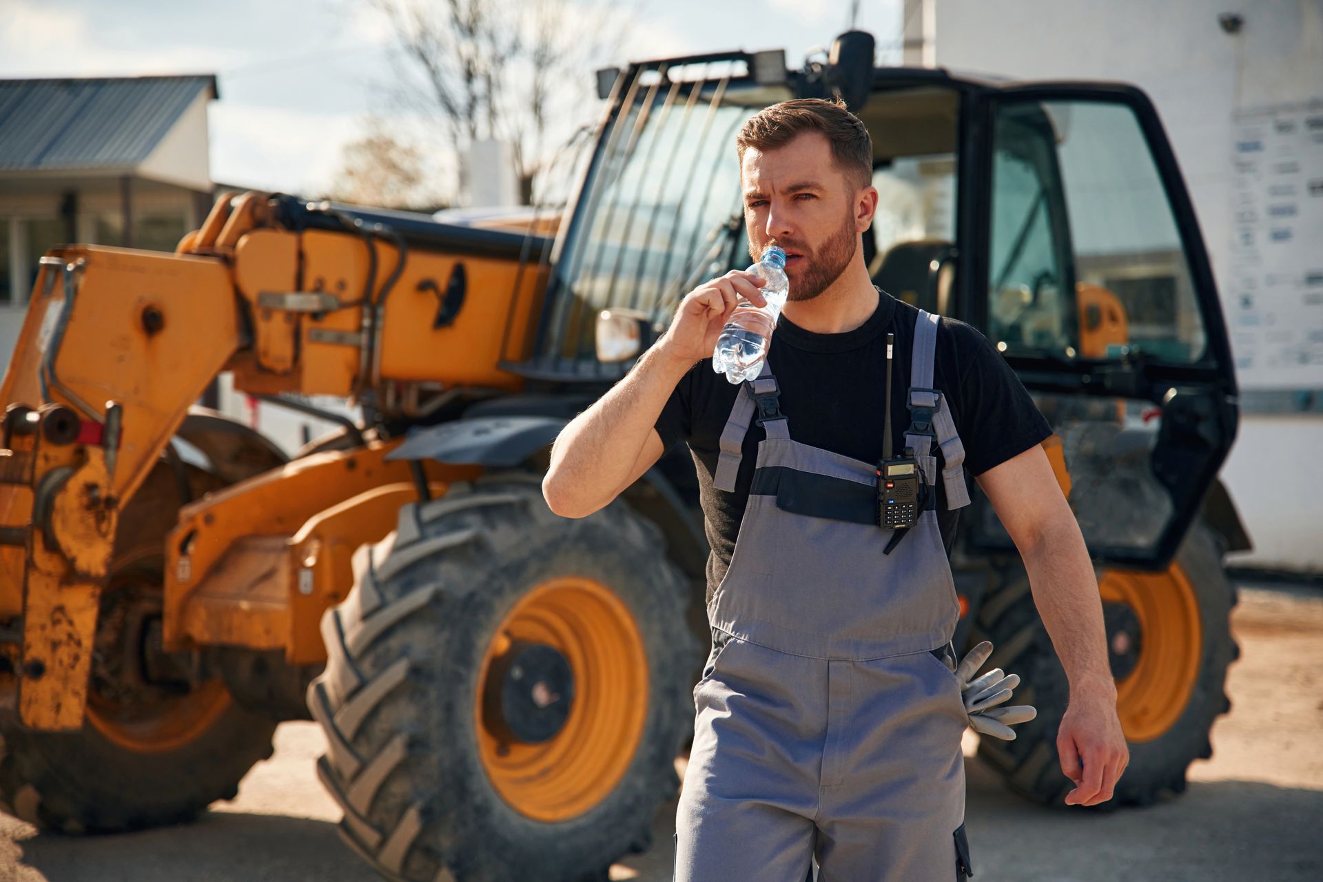 A man is drinking water from a bottle in front of a tractor.