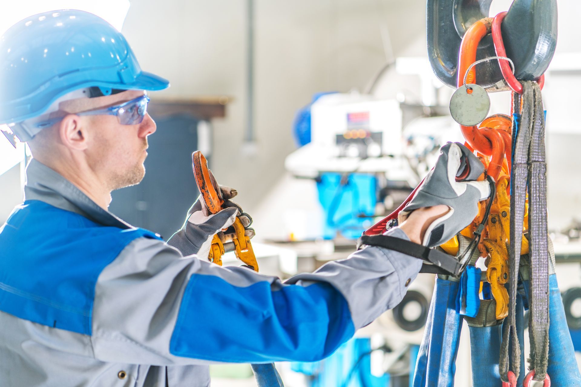 A man wearing a hard hat and safety glasses is working on a crane in a factory.