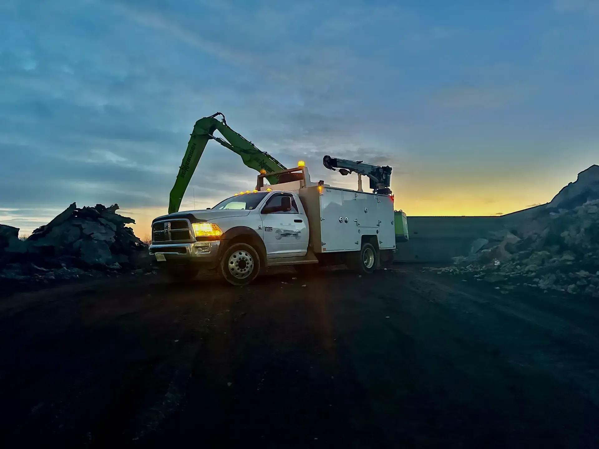 A white truck with a crane on top of it is parked in front of a pile of rocks.