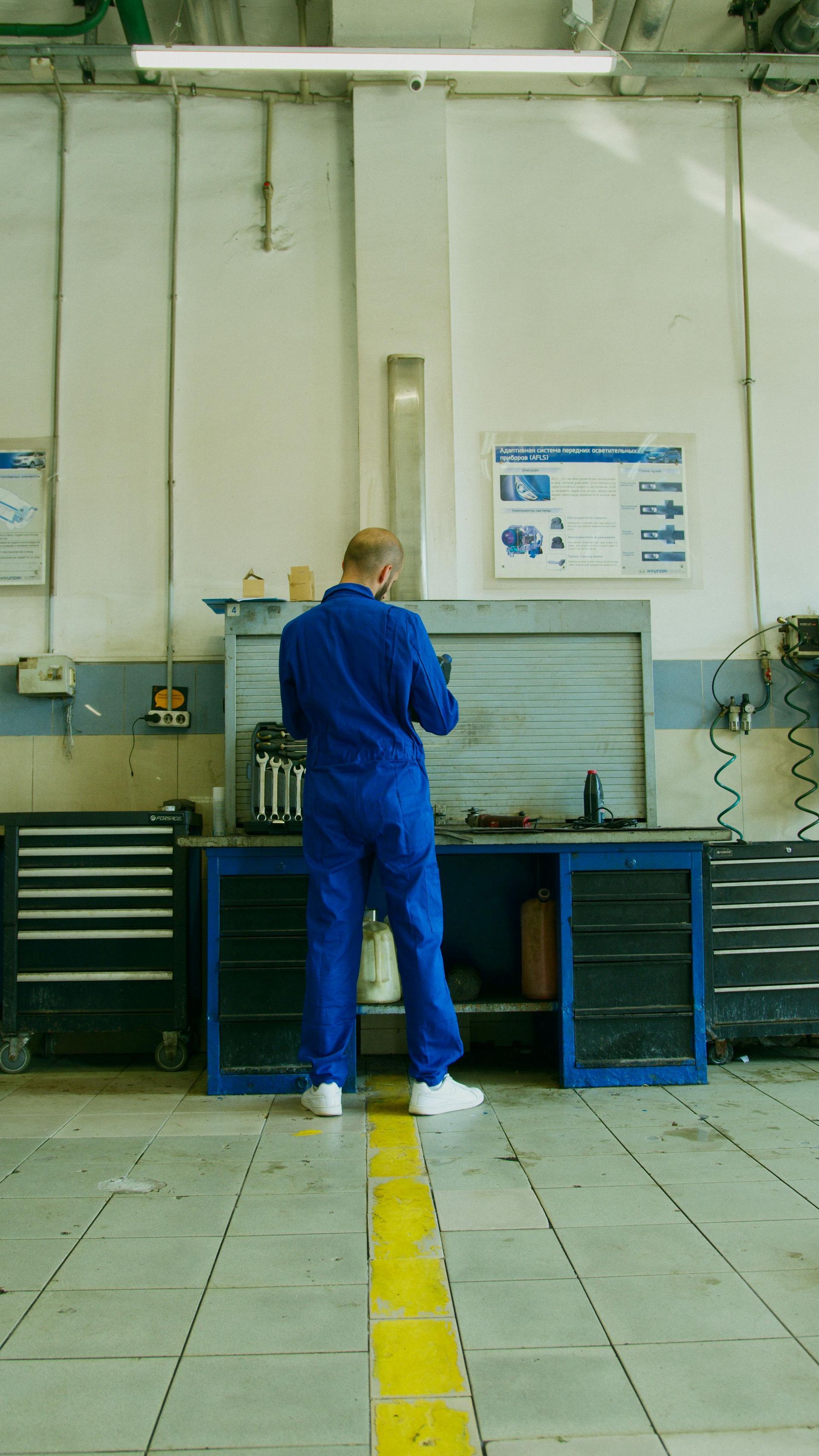 A man in a blue jumpsuit is standing in a garage.