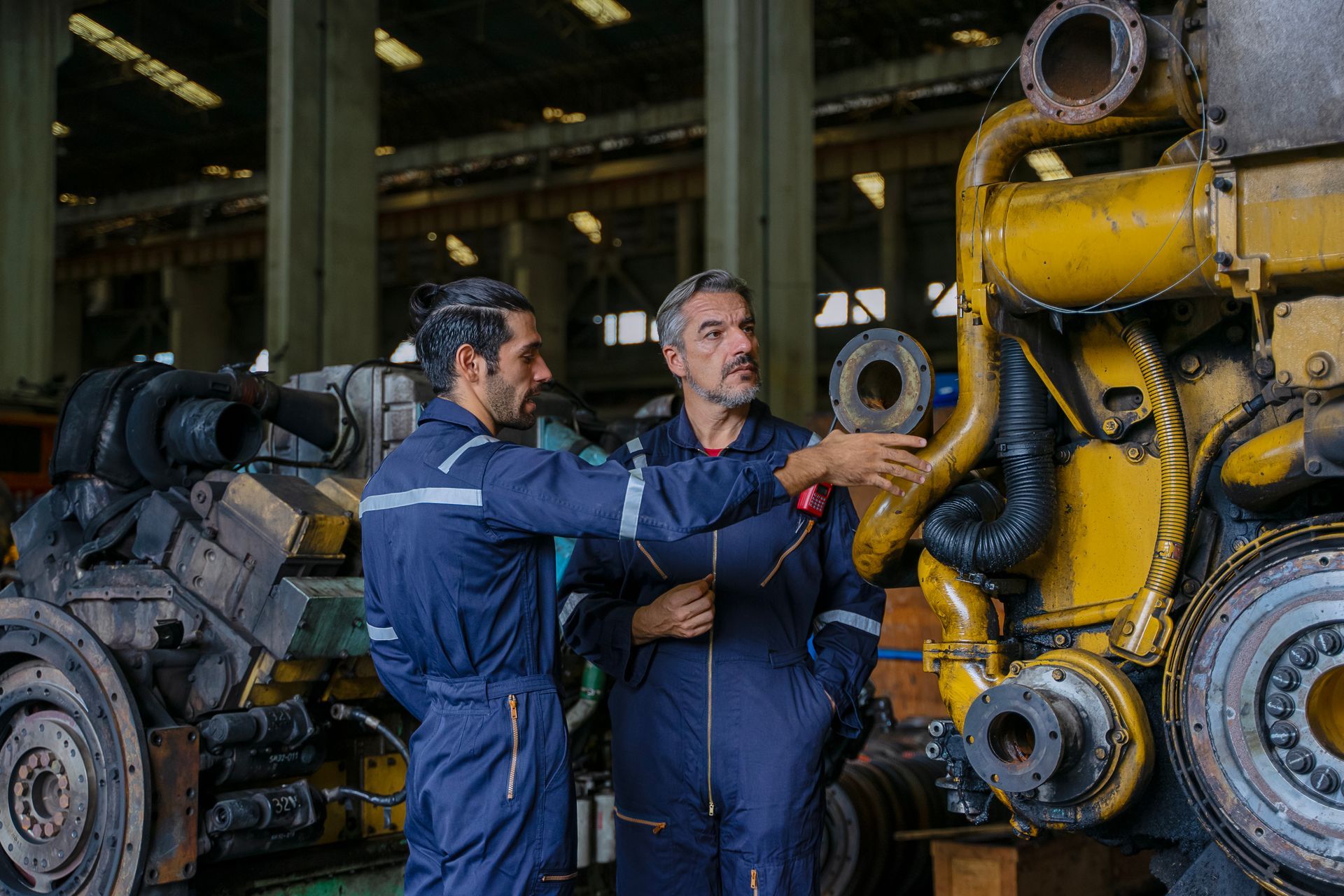 Two men are working on a large engine in a factory.