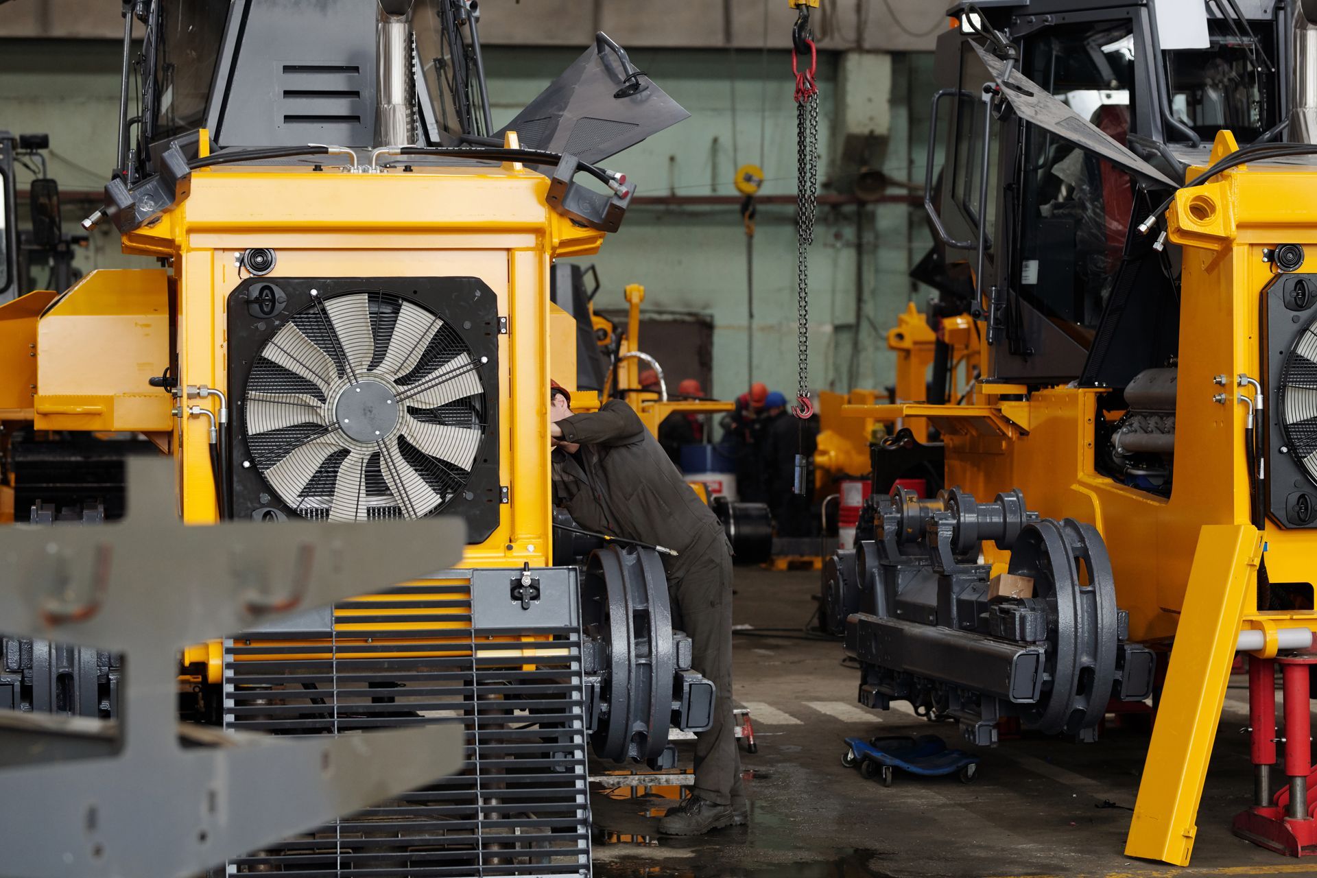 A man is working on a yellow tractor in a factory.