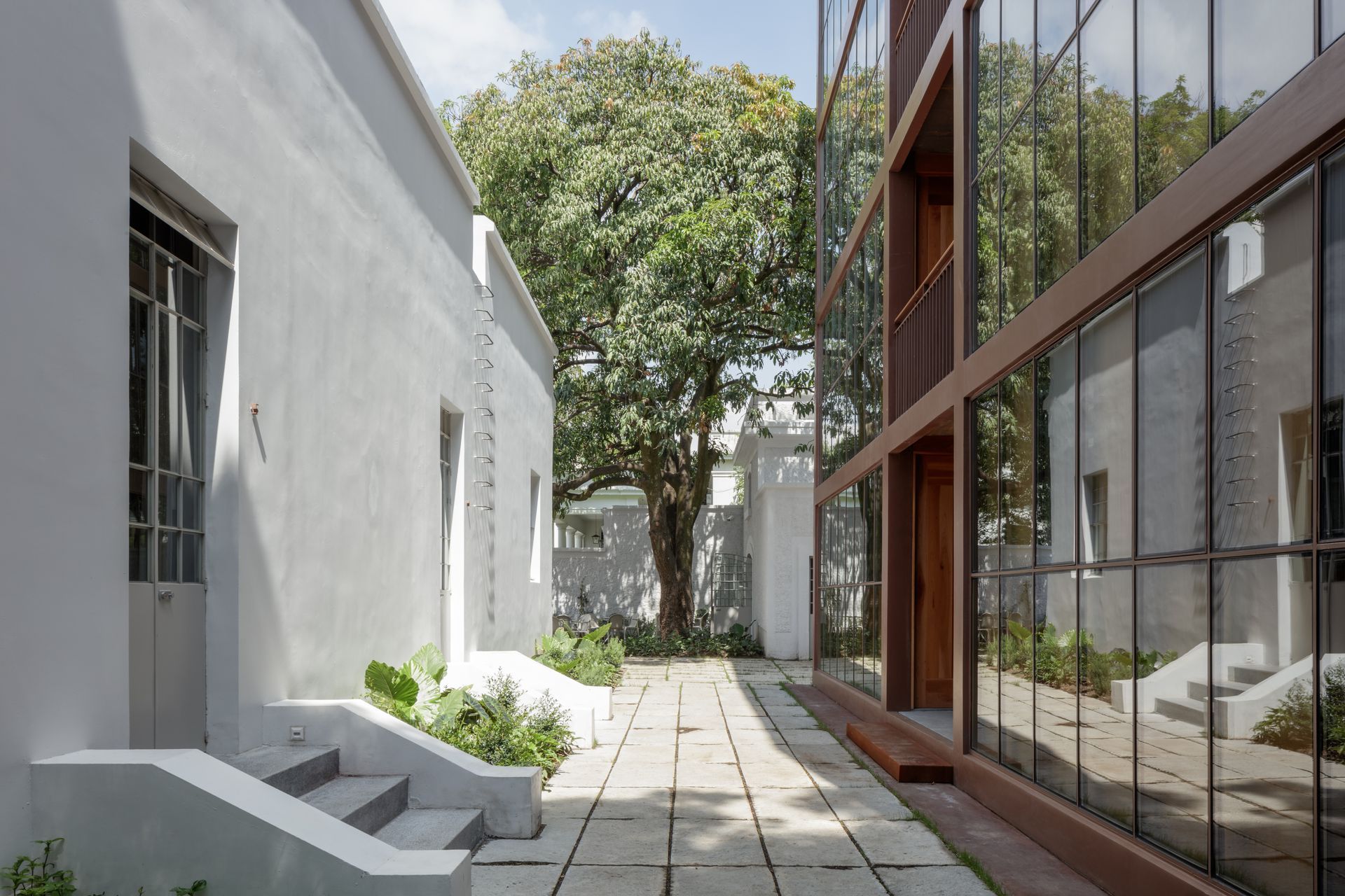 Pathway between white building and modern glass structure, with tree in background.