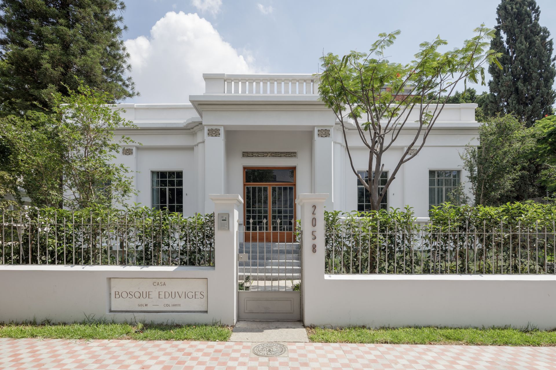 White building with pillars, fenced in with a gate. Trees and greenery around the building.