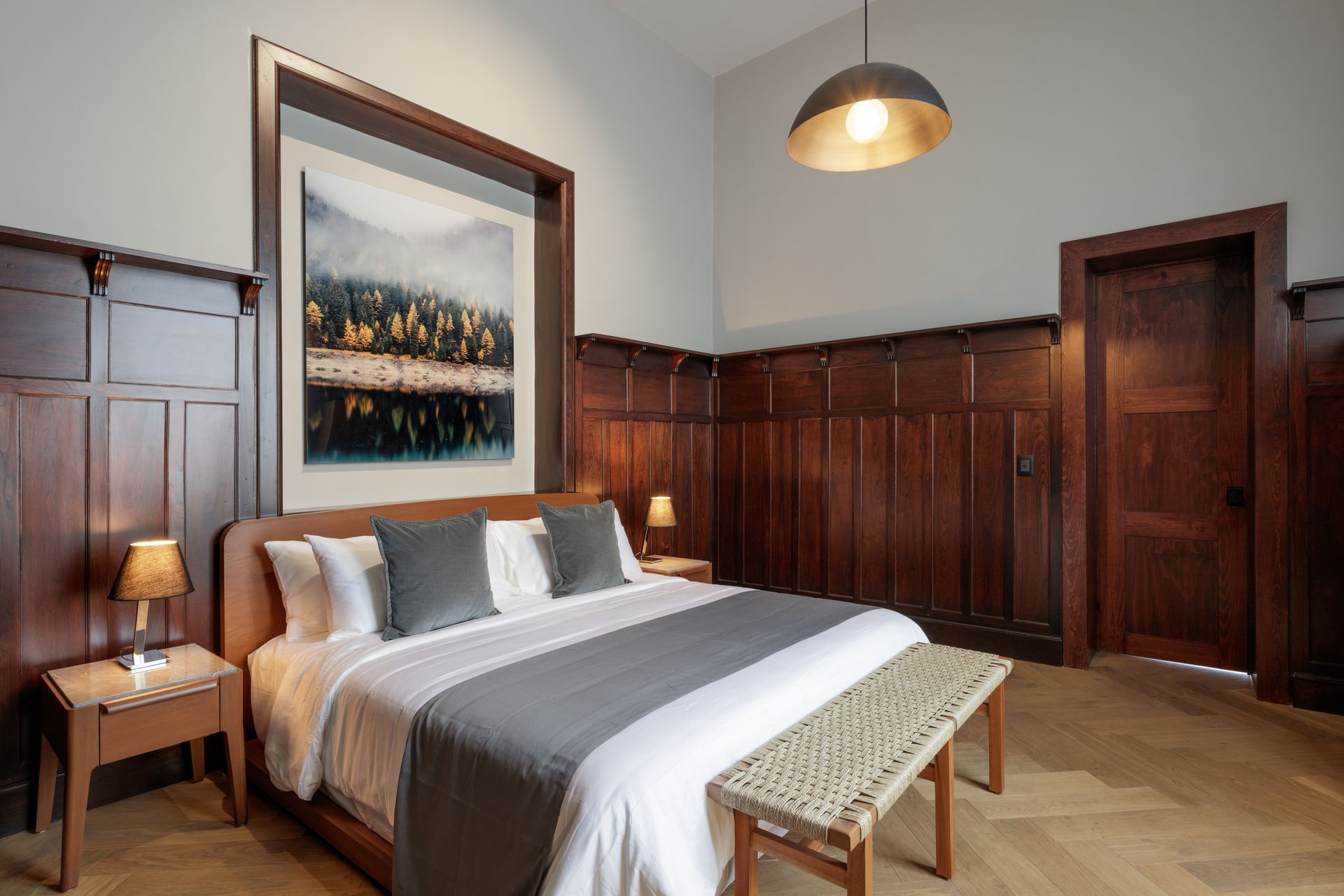 Bedroom with wooden paneling, a bed with gray and white linens, and a landscape painting.