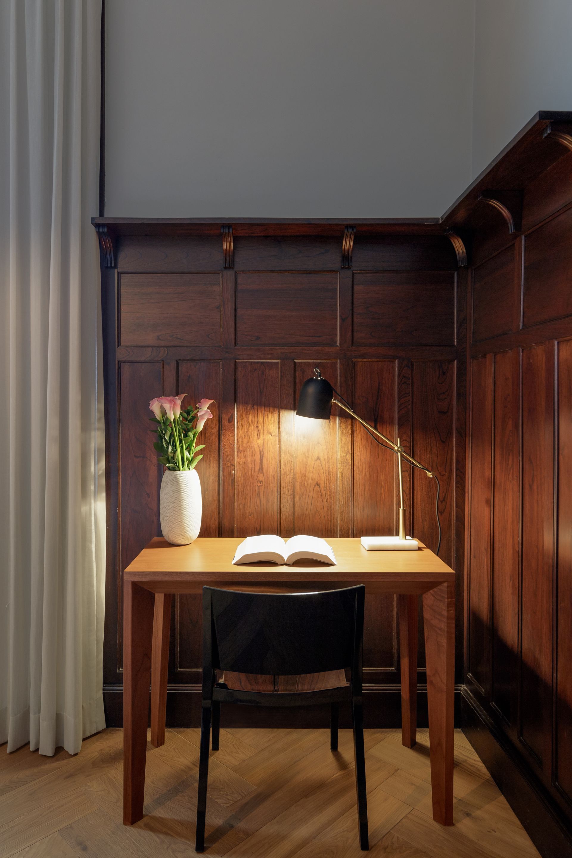 A desk with a lamp and a vase of flowers on it