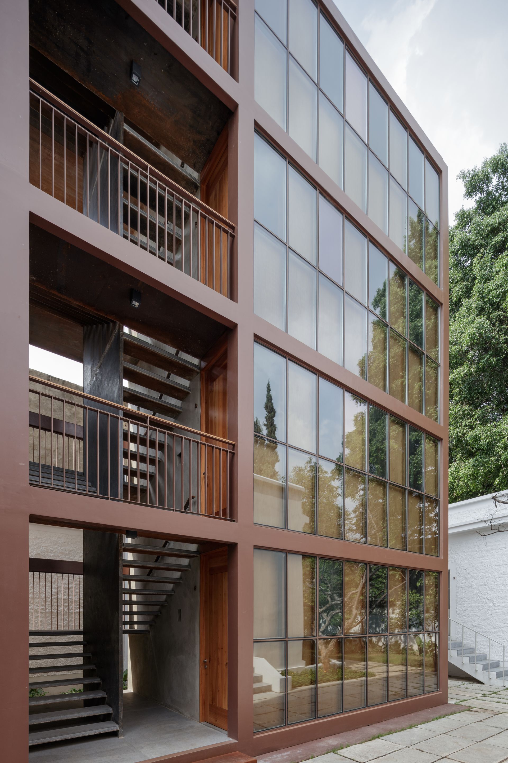 Modern building facade with glass windows and brown frames. Outdoor stairs.