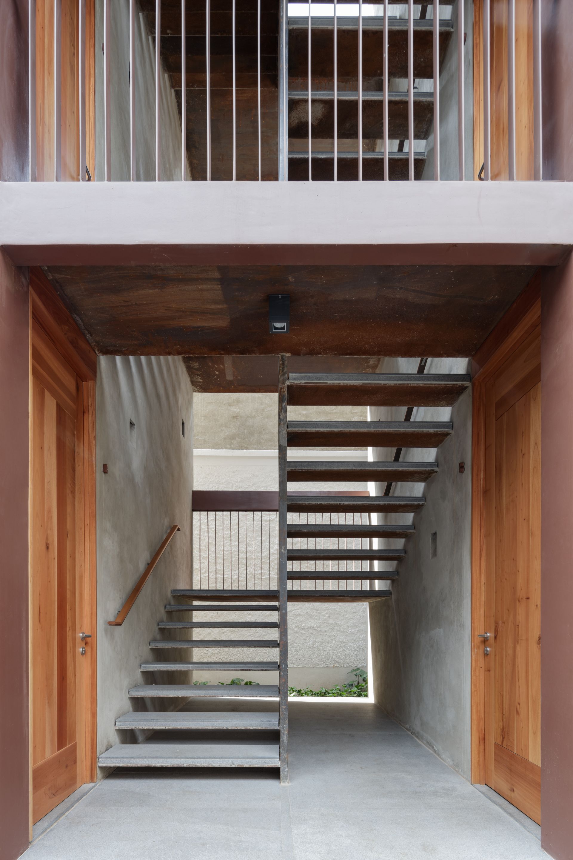 Concrete stairs and hallway, with wood doors and metal railings.