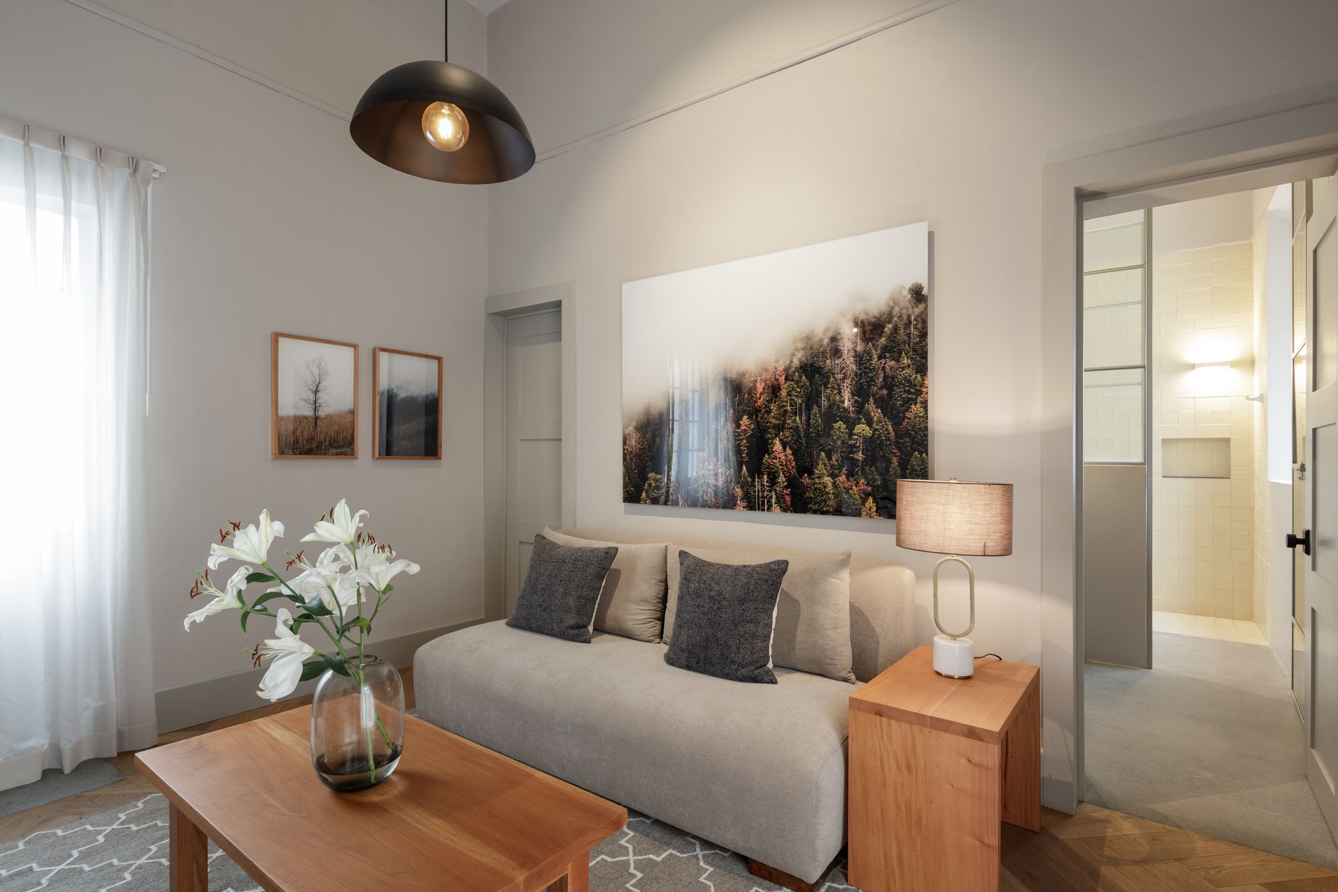 A living room with a couch , coffee table , lamps and a painting on the wall.
