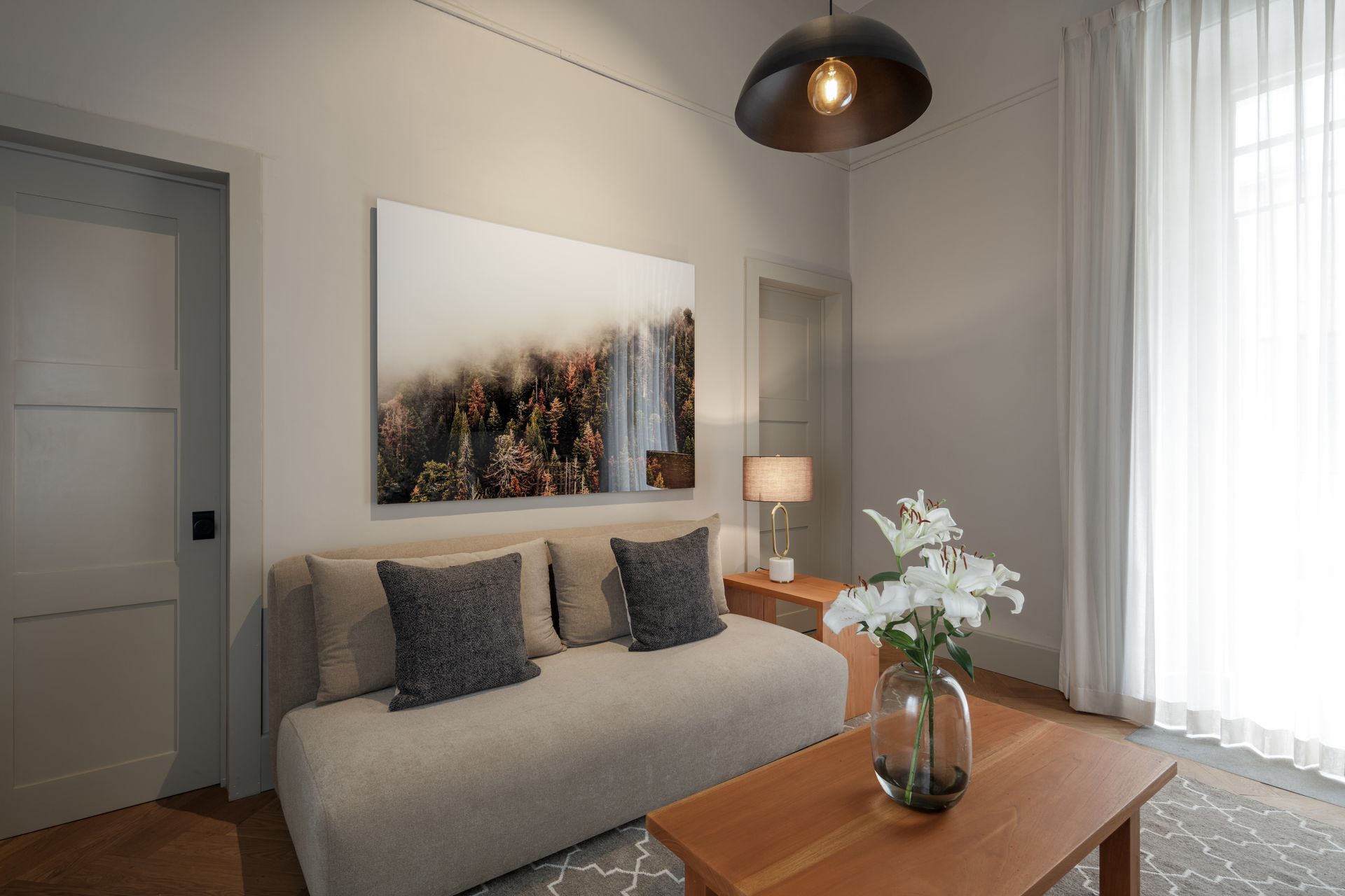 A living room with a couch , coffee table , and a painting on the wall.