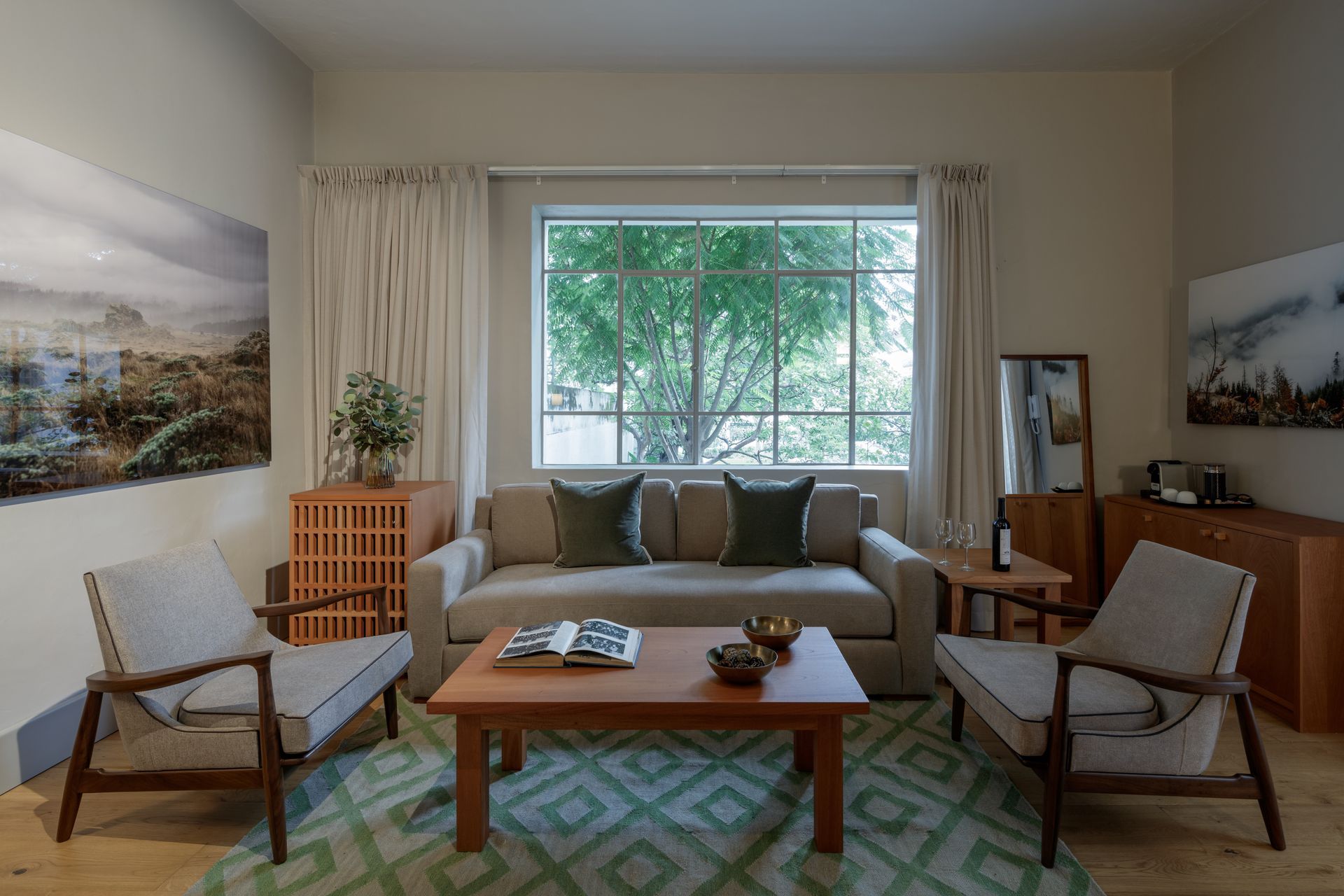 Living room with sofa, armchairs, coffee table, large window, and artwork; light color scheme.