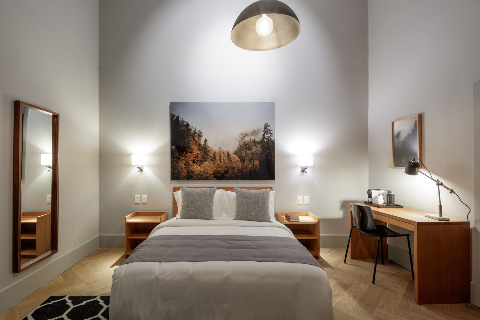 A bedroom with a bed , desk , mirror and painting on the wall.