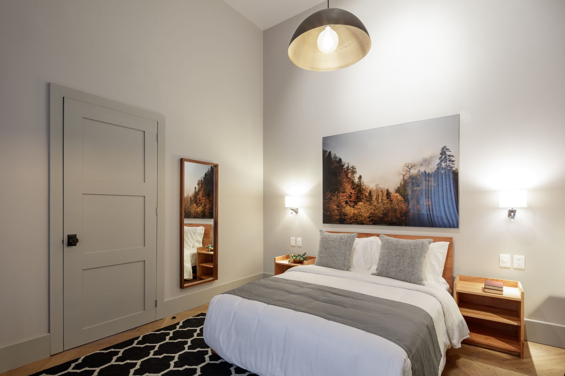 A bedroom with a bed , nightstand , mirror and painting on the wall.