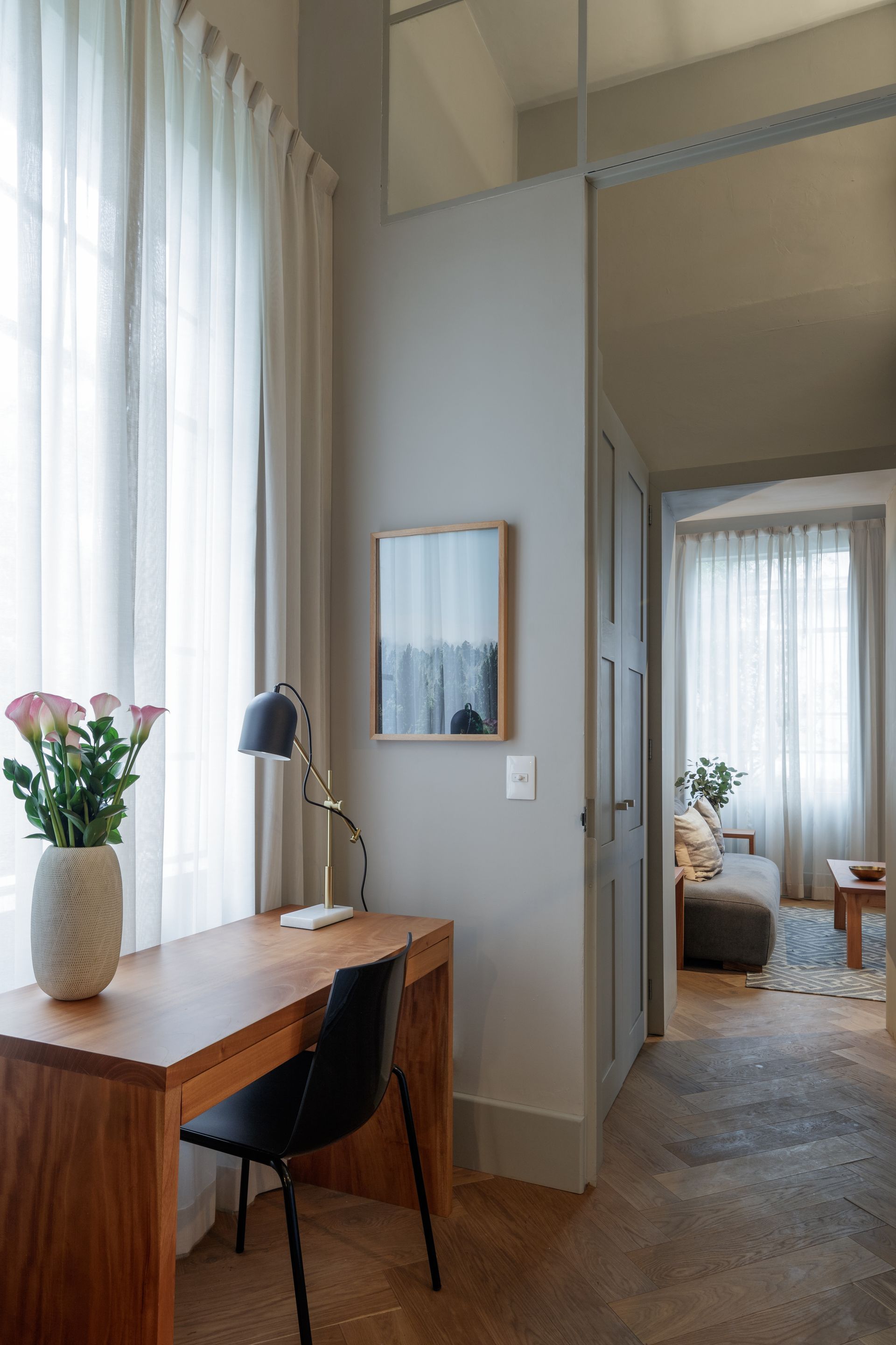 A room with a desk , chair , lamp and mirror.