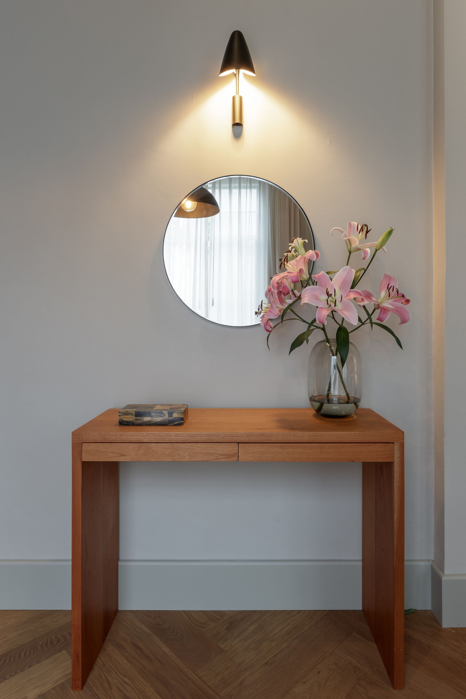 A wooden table with a vase of flowers on it in front of a mirror.