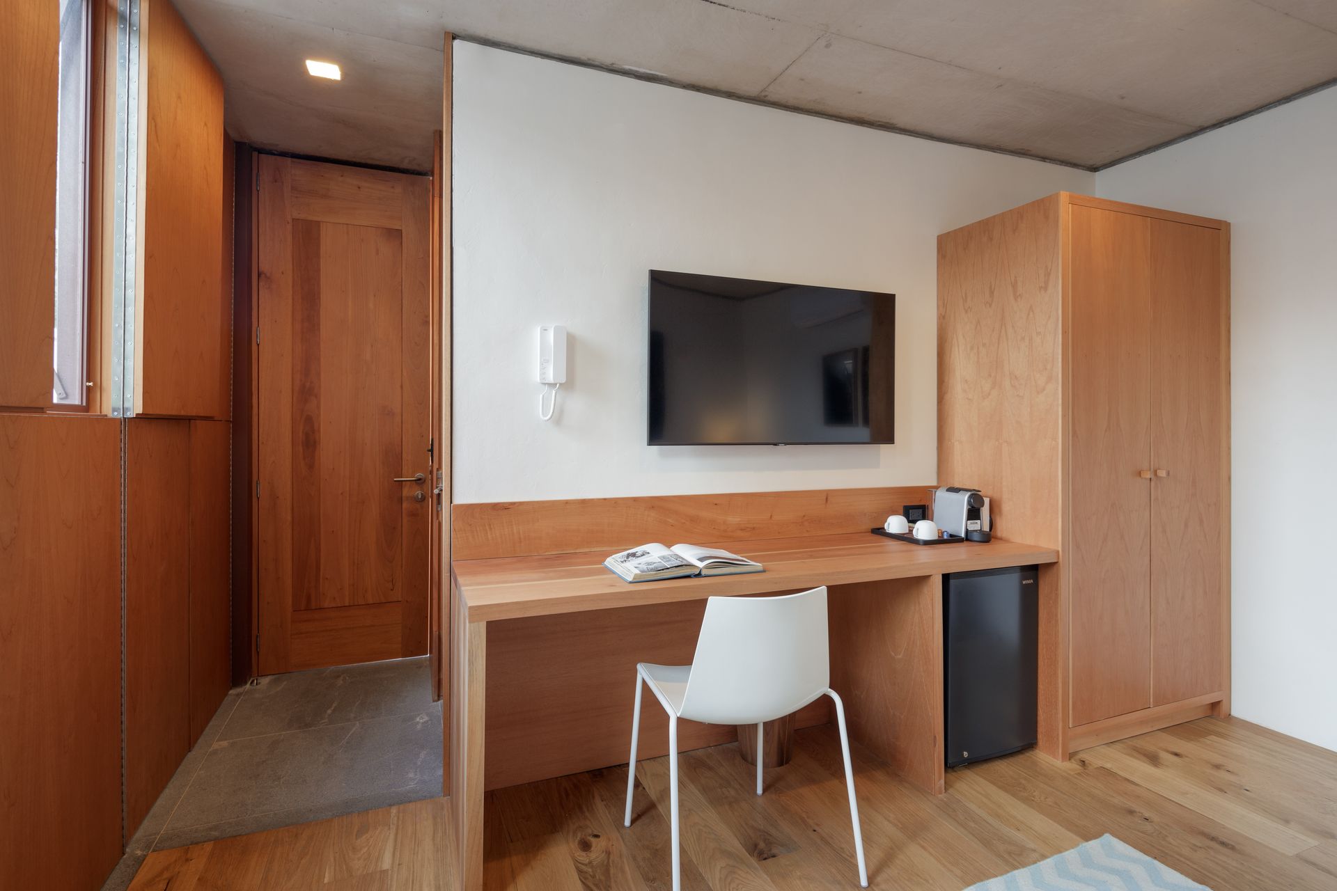A room with a desk and chair and a flat screen tv on the wall.