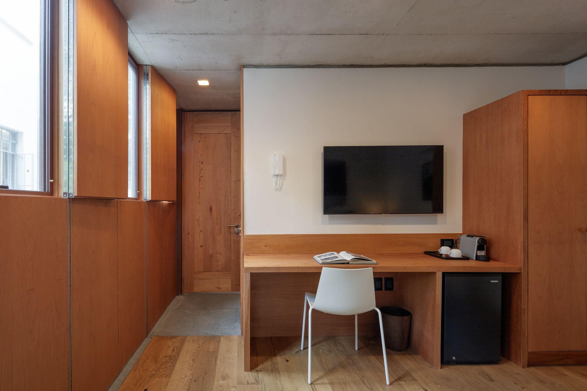 A room with a desk and chair and a flat screen tv on the wall