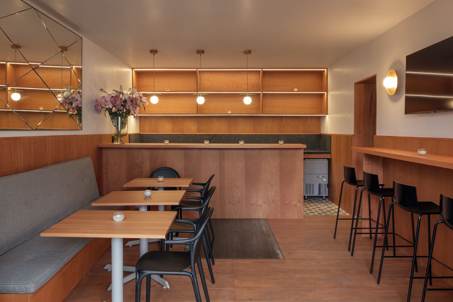 Interior of a bar with wooden accents, tables, seating, and shelves.