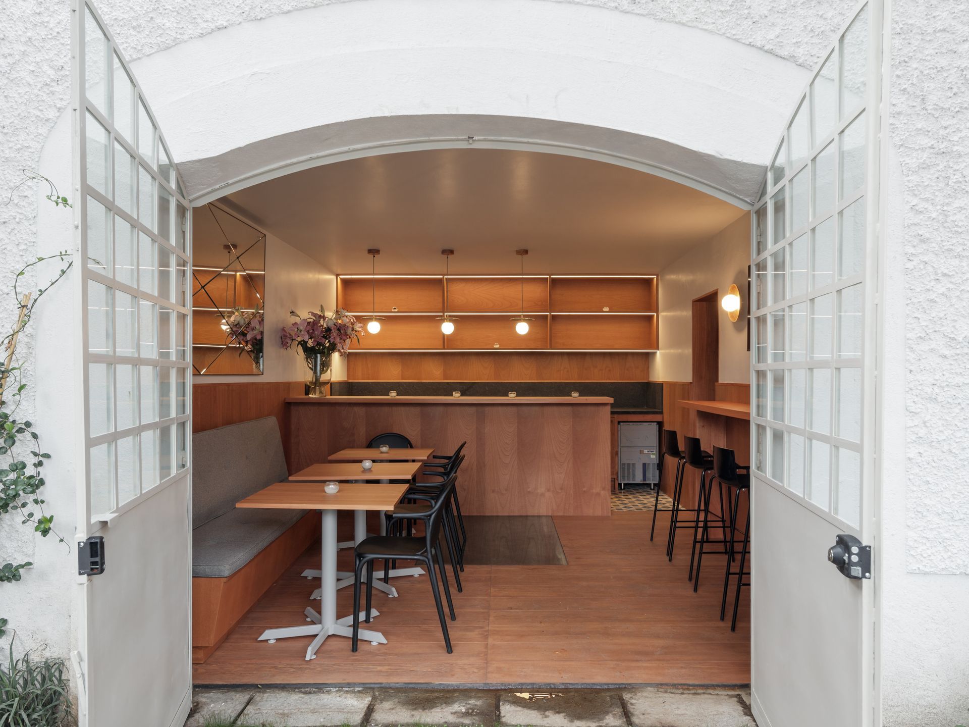 Cafe interior viewed through open white doors, featuring wooden counter, tables, and seating.