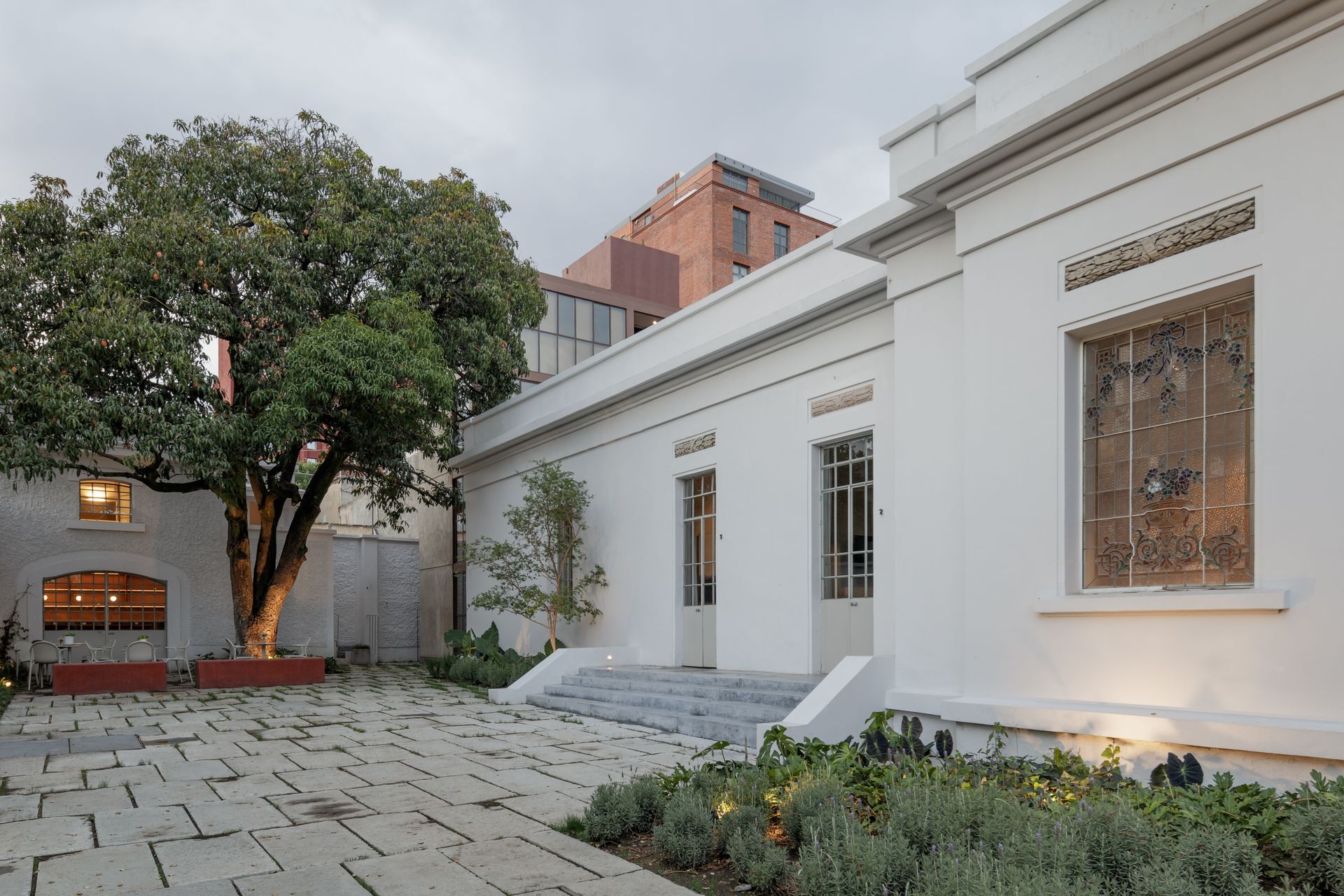 White building with stone patio and a large tree.