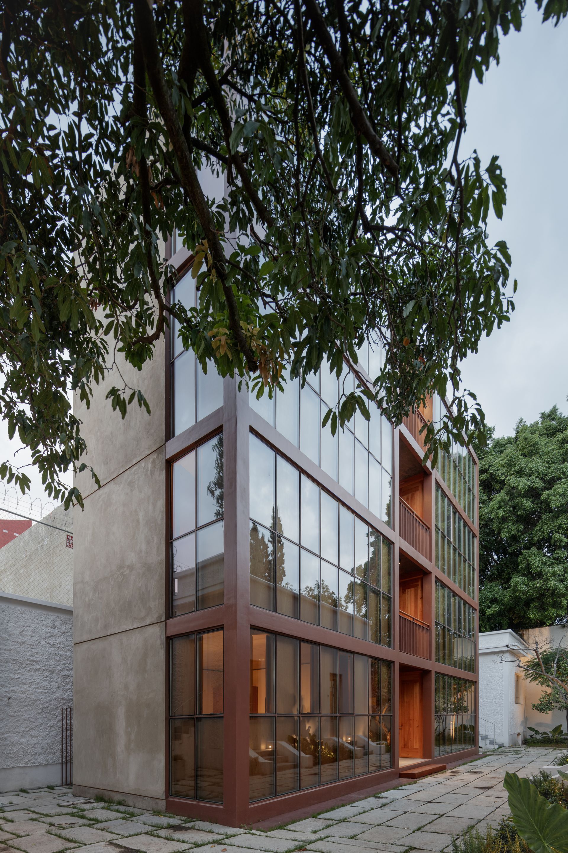 Modern building with glass facade and brown frame, partially obscured by a tree.