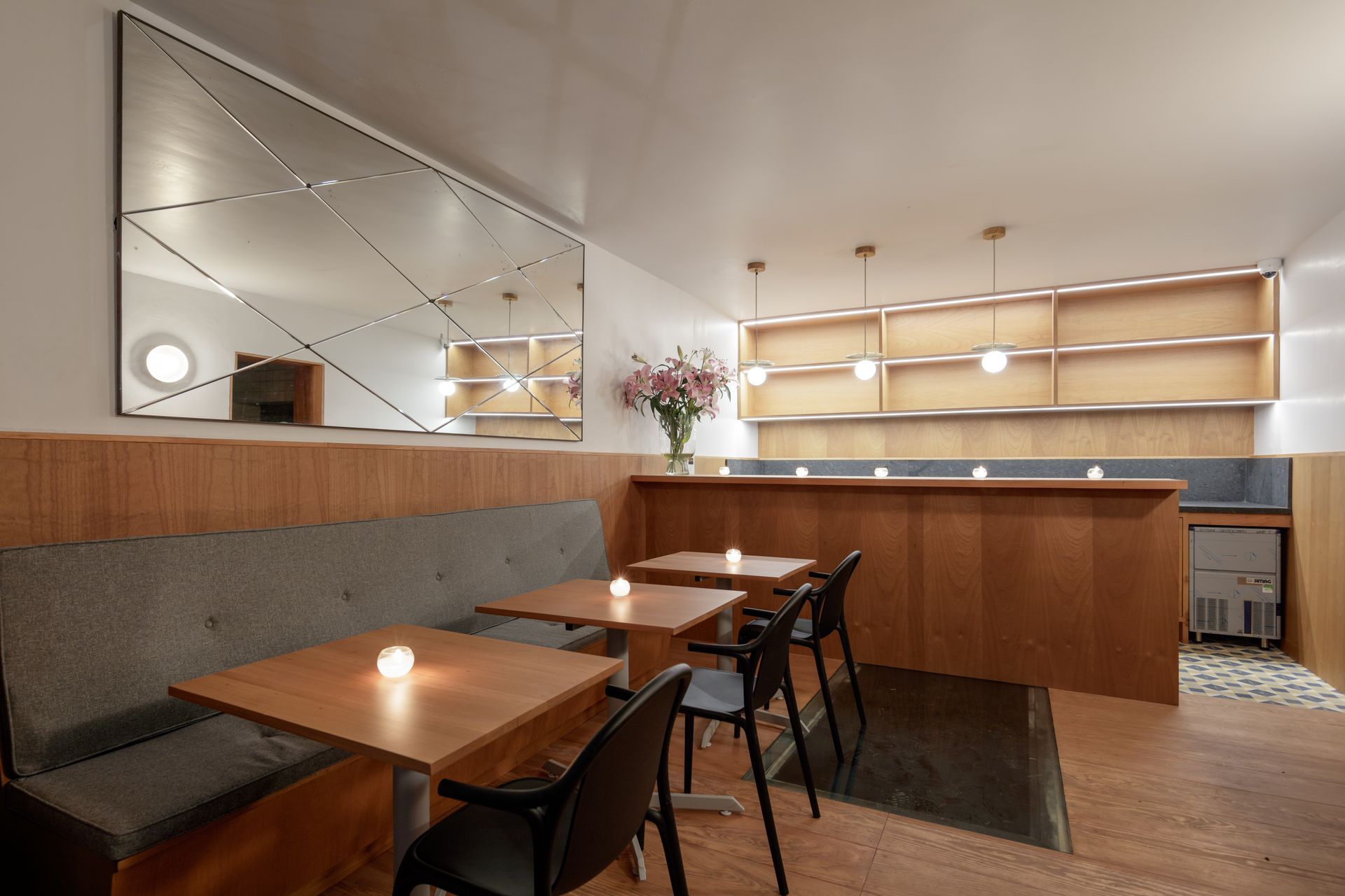 Interior of a cafe with tables, a banquette, and a decorative mirror on the wall.