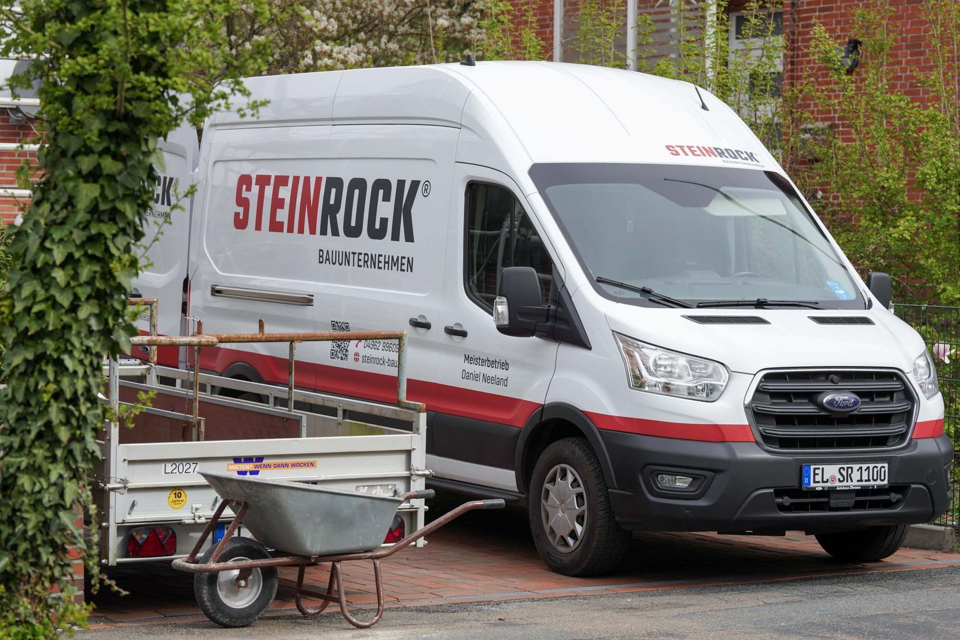 Ein Steinrock Firmenfahrzeug parkt vor einem Backsteingebäude, davor steht ein kleiner Anhänger.