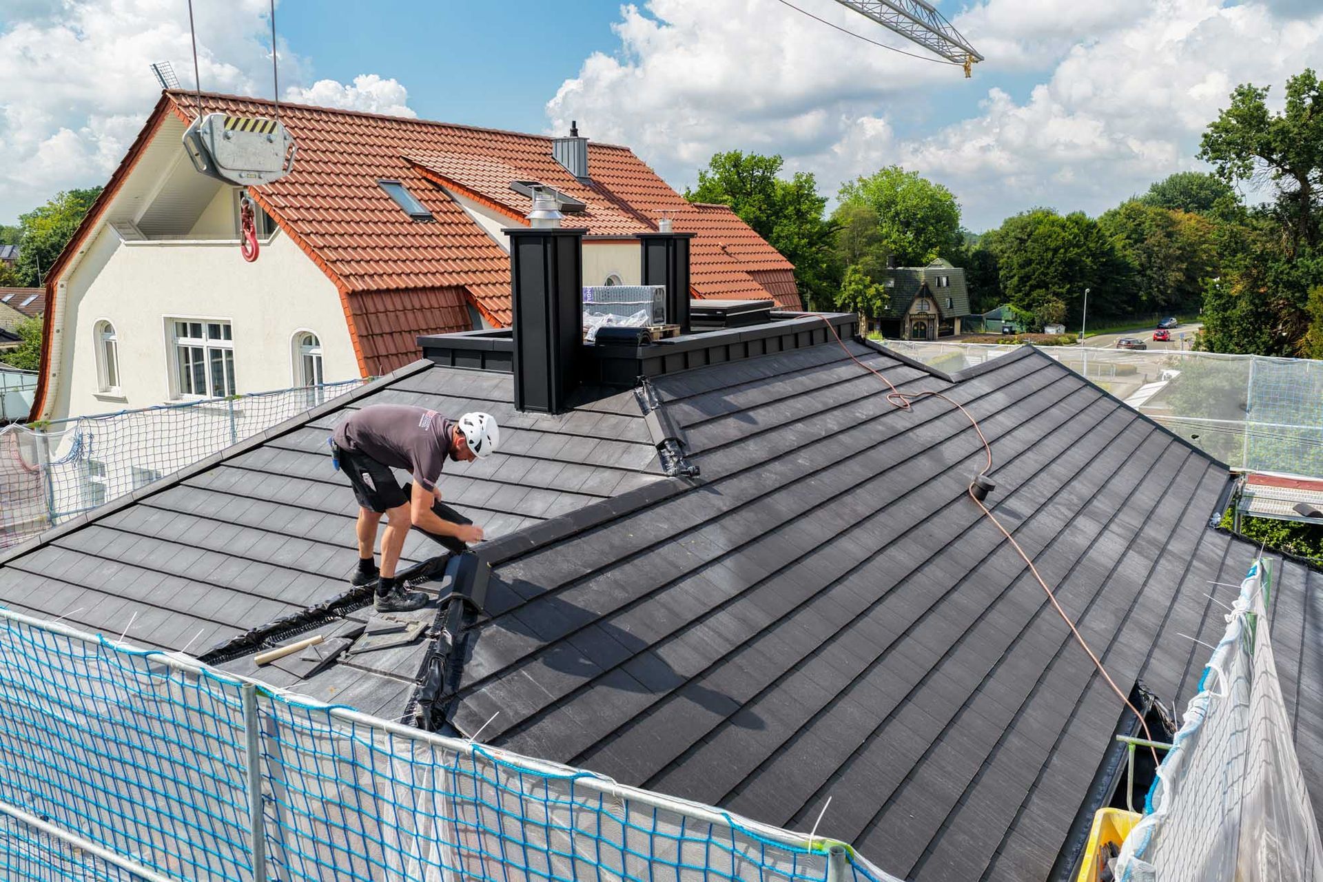 Arbeiter montiert dunkle Metalldachplatten auf einem Hausdach unter hellem Himmel