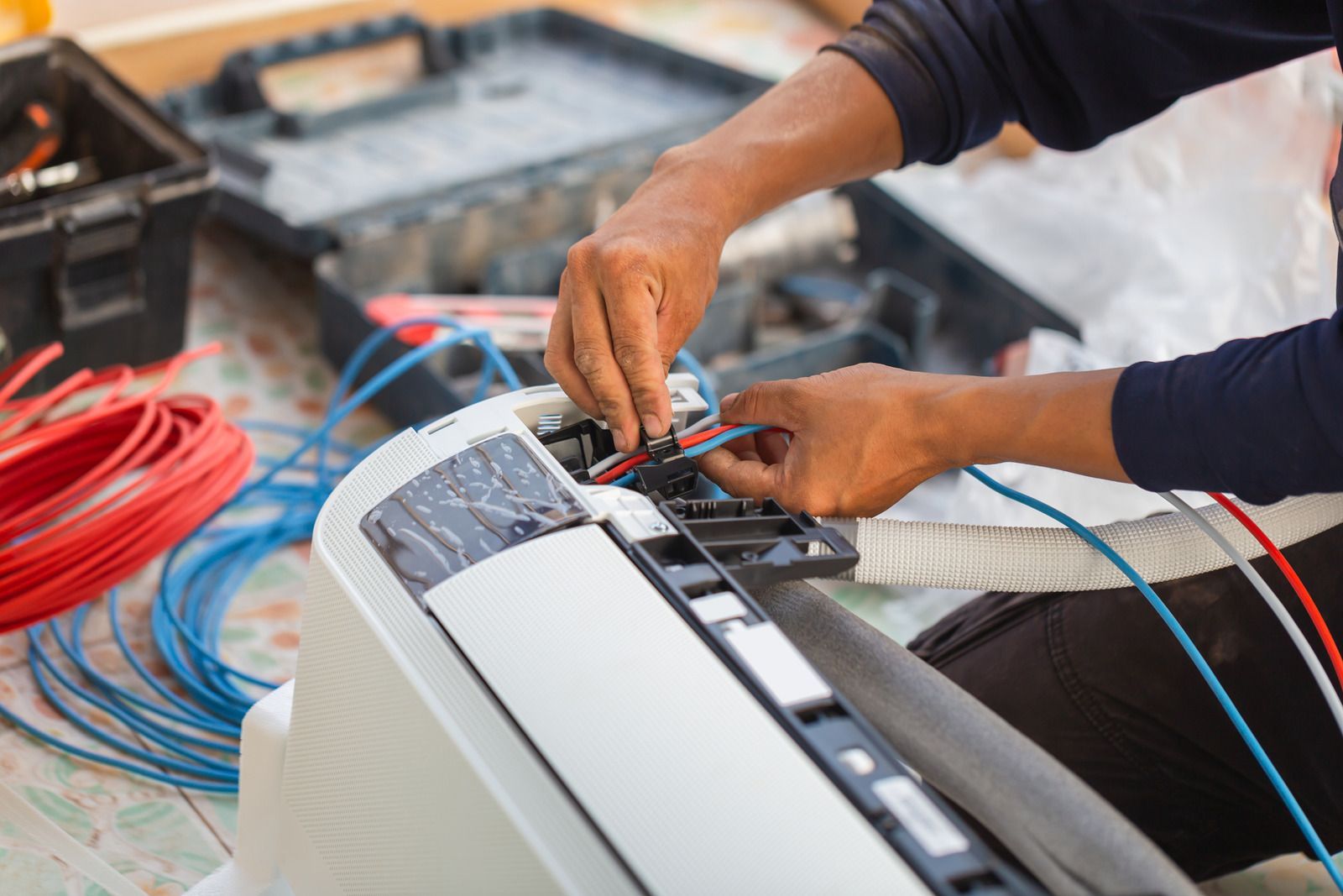 Hands of a person wiring an air conditioning unit; tools and wires are nearby.