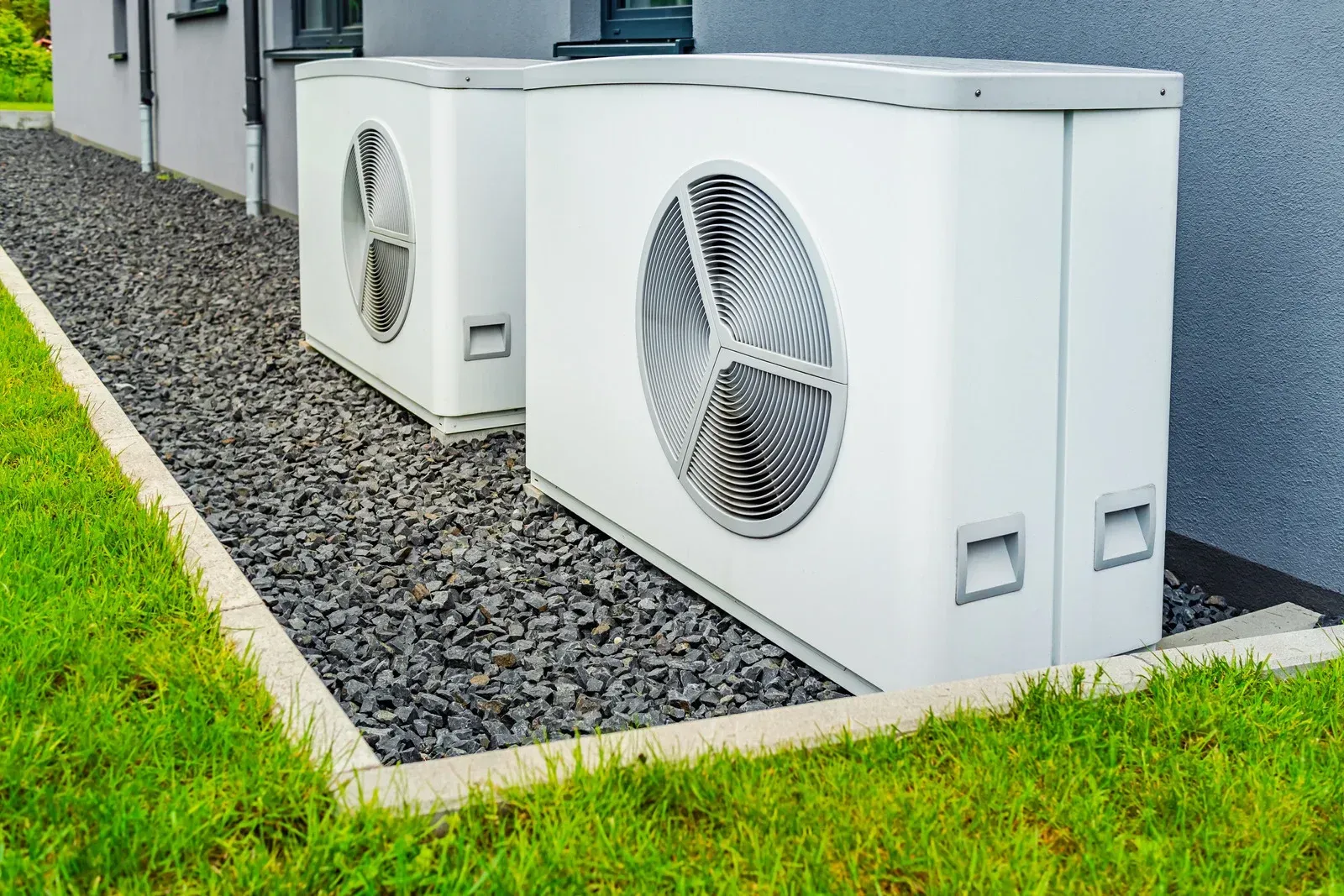 Two air conditioners are sitting next to each other on the side of a building.